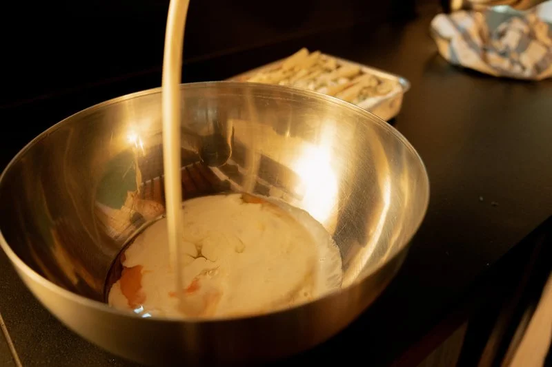 Milk being poured into a stainless steel mixing bowl.