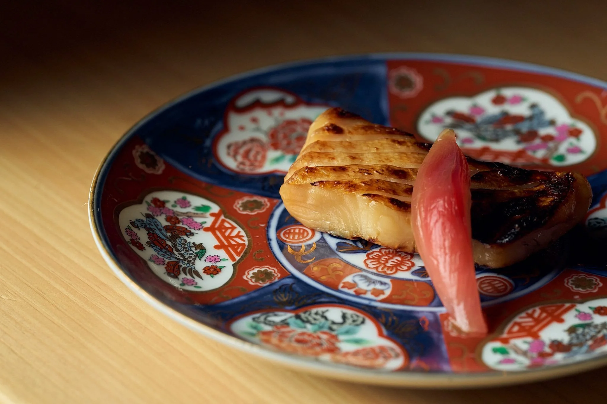 A colorful Japanese-style plate with grilled fish and a pickled ginger slice.