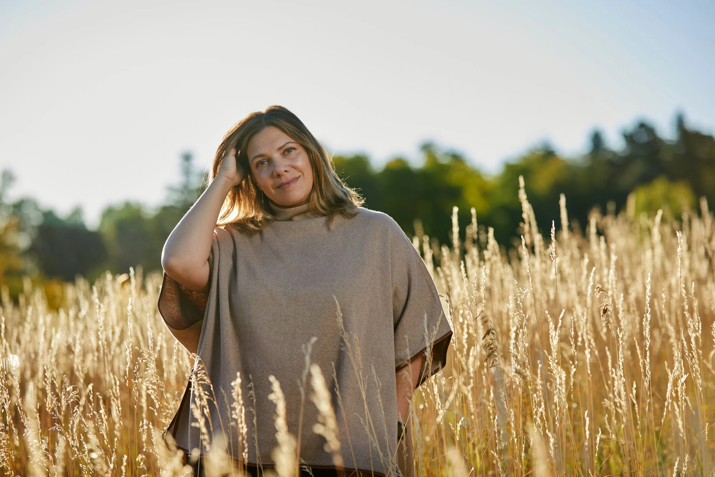 Woman standing in a field of tall, golden grass with trees in the background and a blue sky overhead feeling renewed.