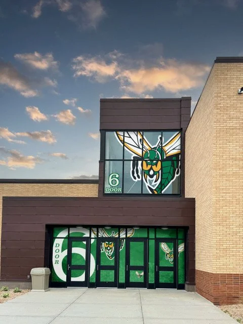 Glass doors with a green and black illustration of a hornet or wasp above the entrance, with the number 6 and the word "Door" written on them.