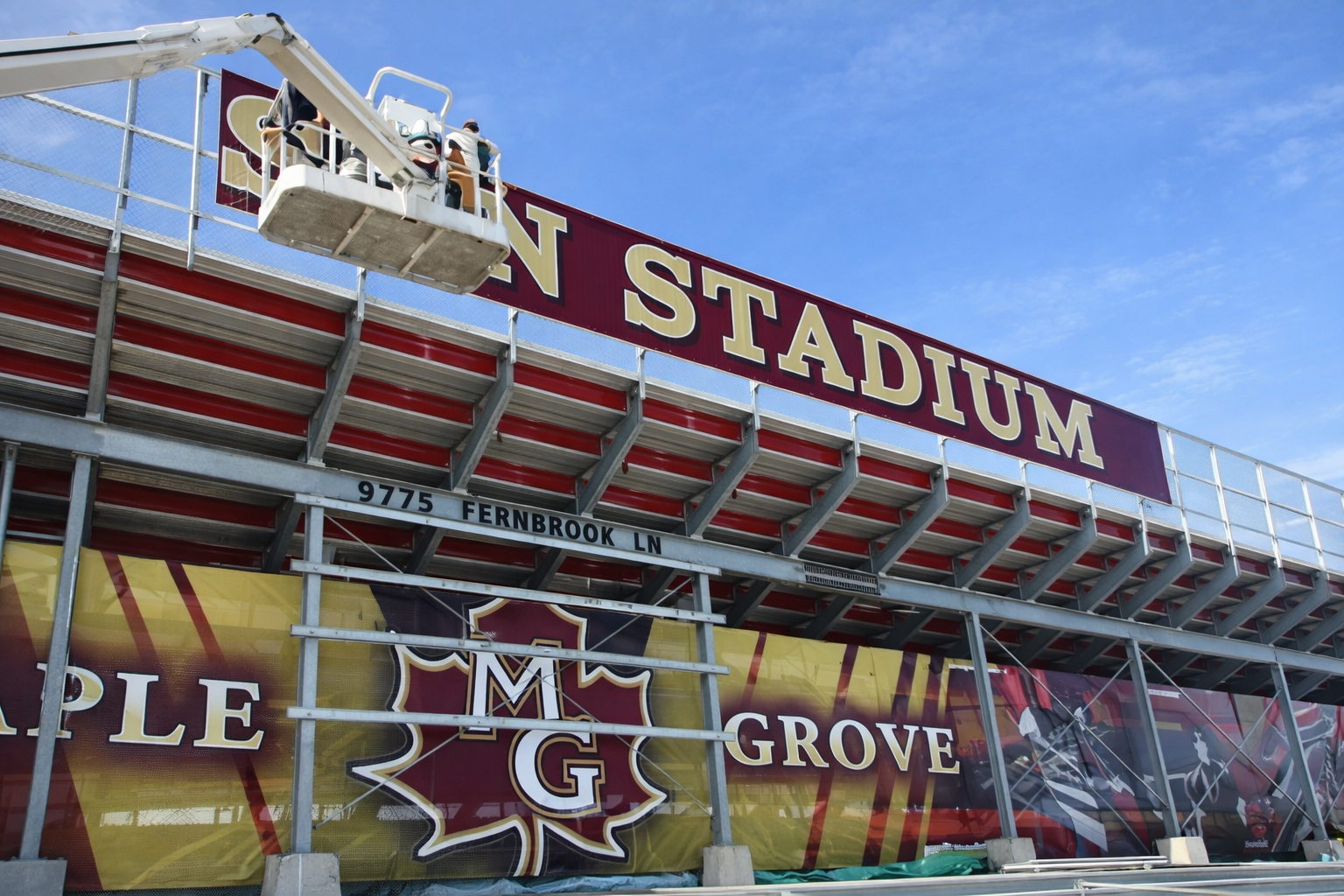 View of a stadium entrance with a large sign that reads 'STADIUM,' with people on a lift working on the sign.