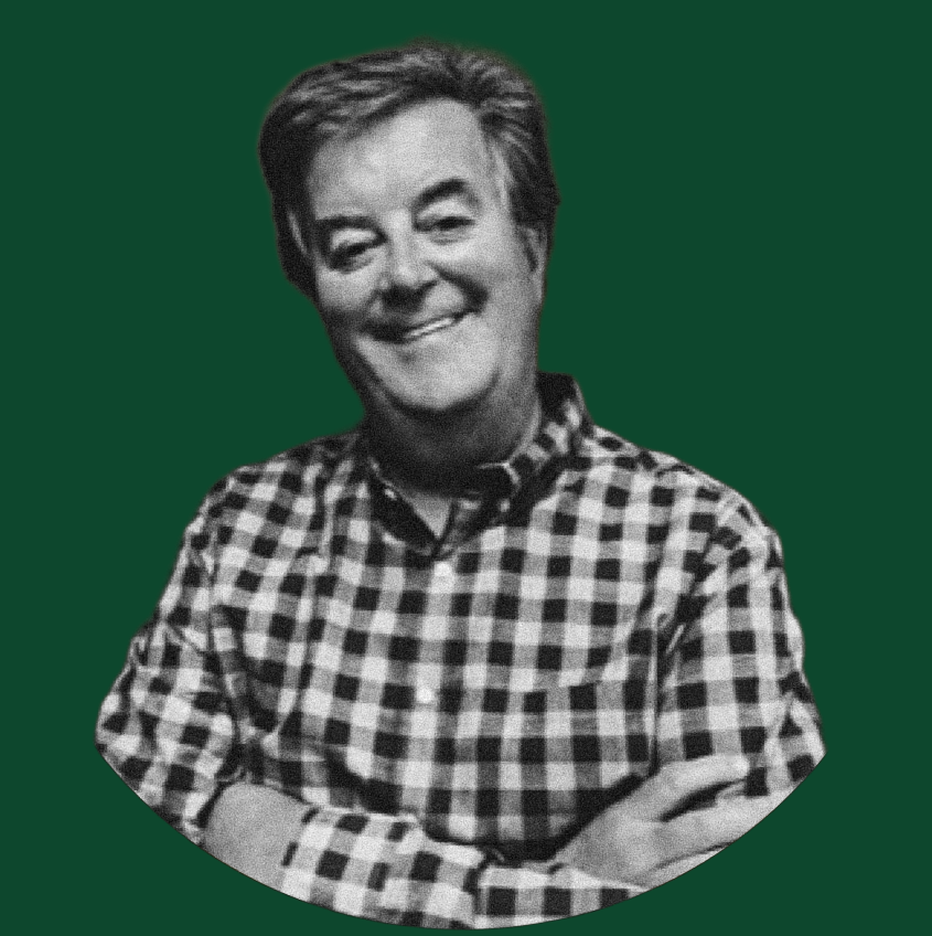 A black and white photo of a smiling person wearing a checkered shirt, with arms crossed, against a solid dark green background.