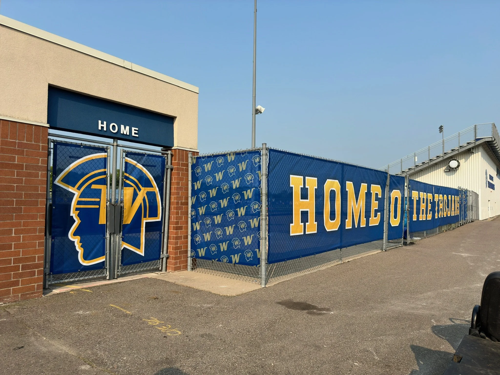 Entrance gate to a sports field with banners displaying the words 'HOME OF THE TITANS' and a logo of a head in a helmet.