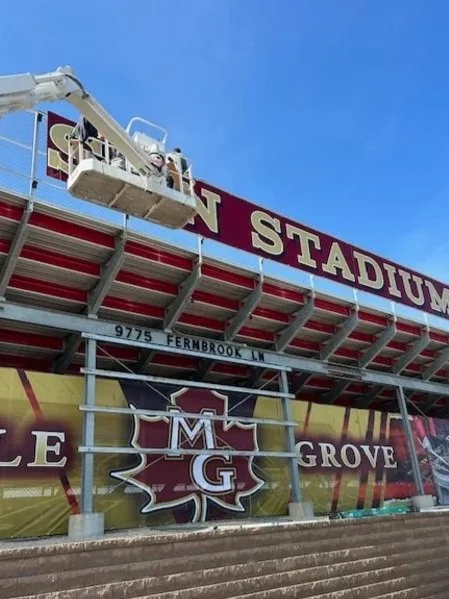 A construction worker on a cherry picker working on a stadium sign that reads 'STADIUM'.