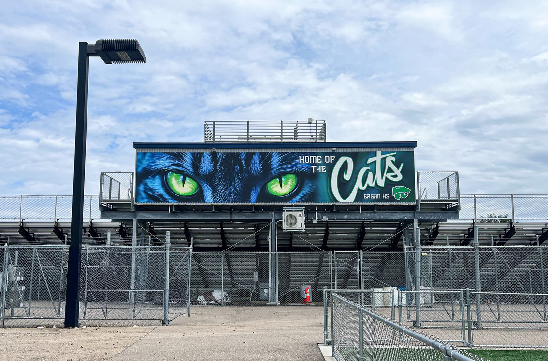 A sports stadium with a large sign that shows a cat with green eyes, the text 'Home of the Cats,' and the logo of Eagan High School.