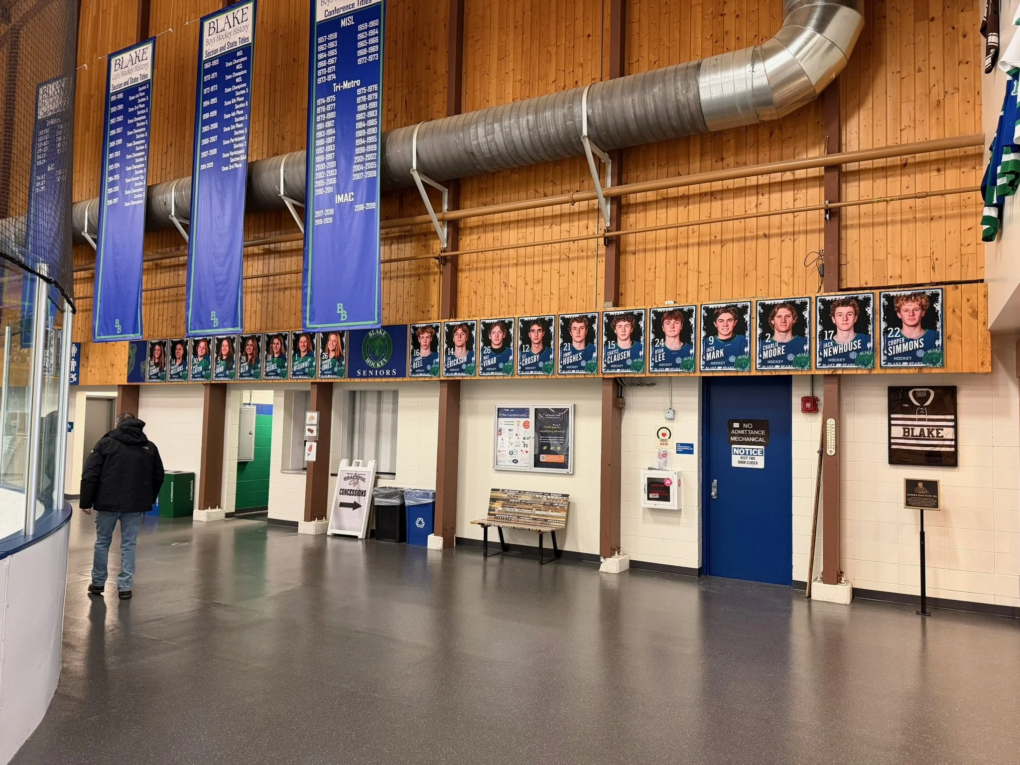 Indoor hockey arena lobby with banners and portraits of players, some doors, and informational signs.