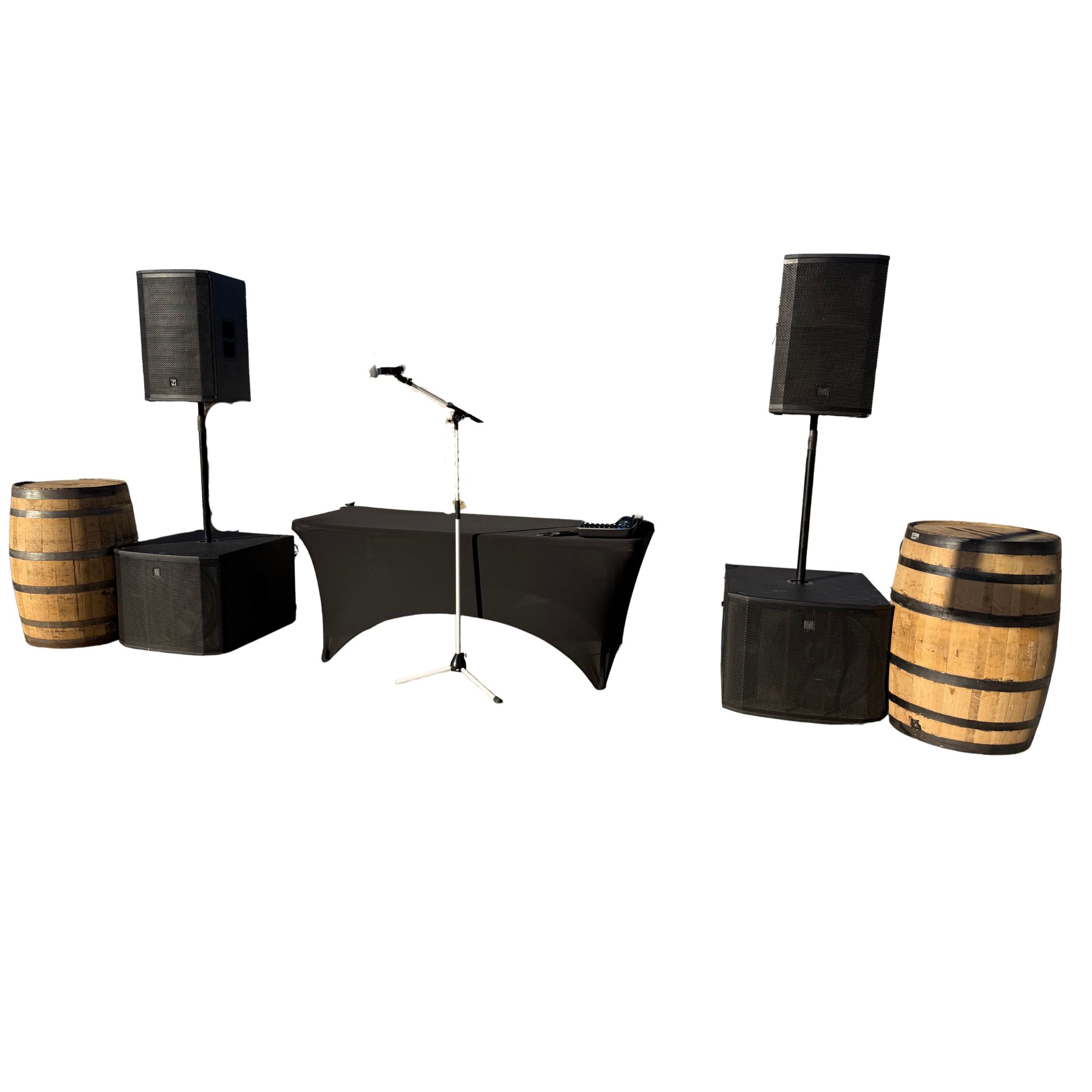 DJ equipment setup with two large speakers on stands, a DJ mixer on a table with a black cloth cover, a microphone on a stand, and two barrels.