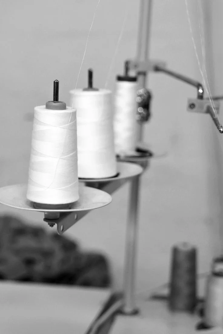 Three spools of white sewing thread on a machine in a sewing workshop.