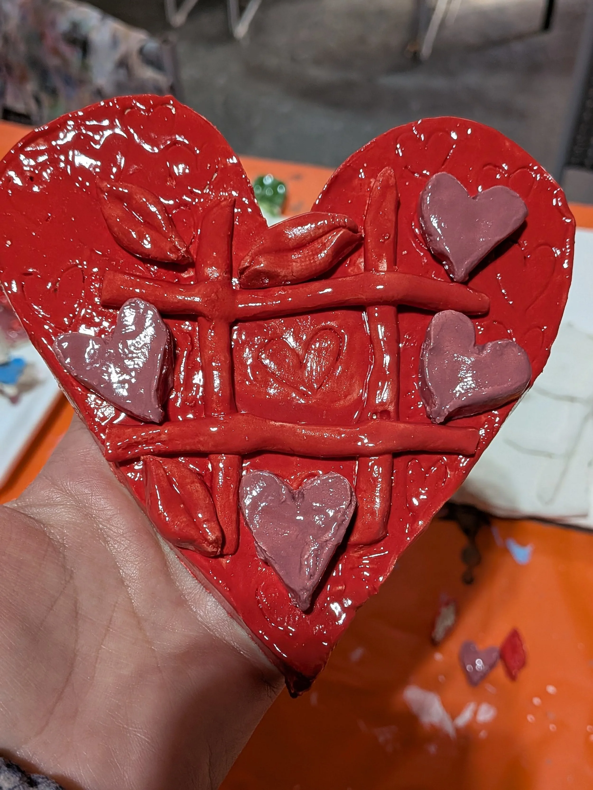 A red heart-shaped object with a textured surface, decorated with small pink heart shapes and a ribbon design in the center.