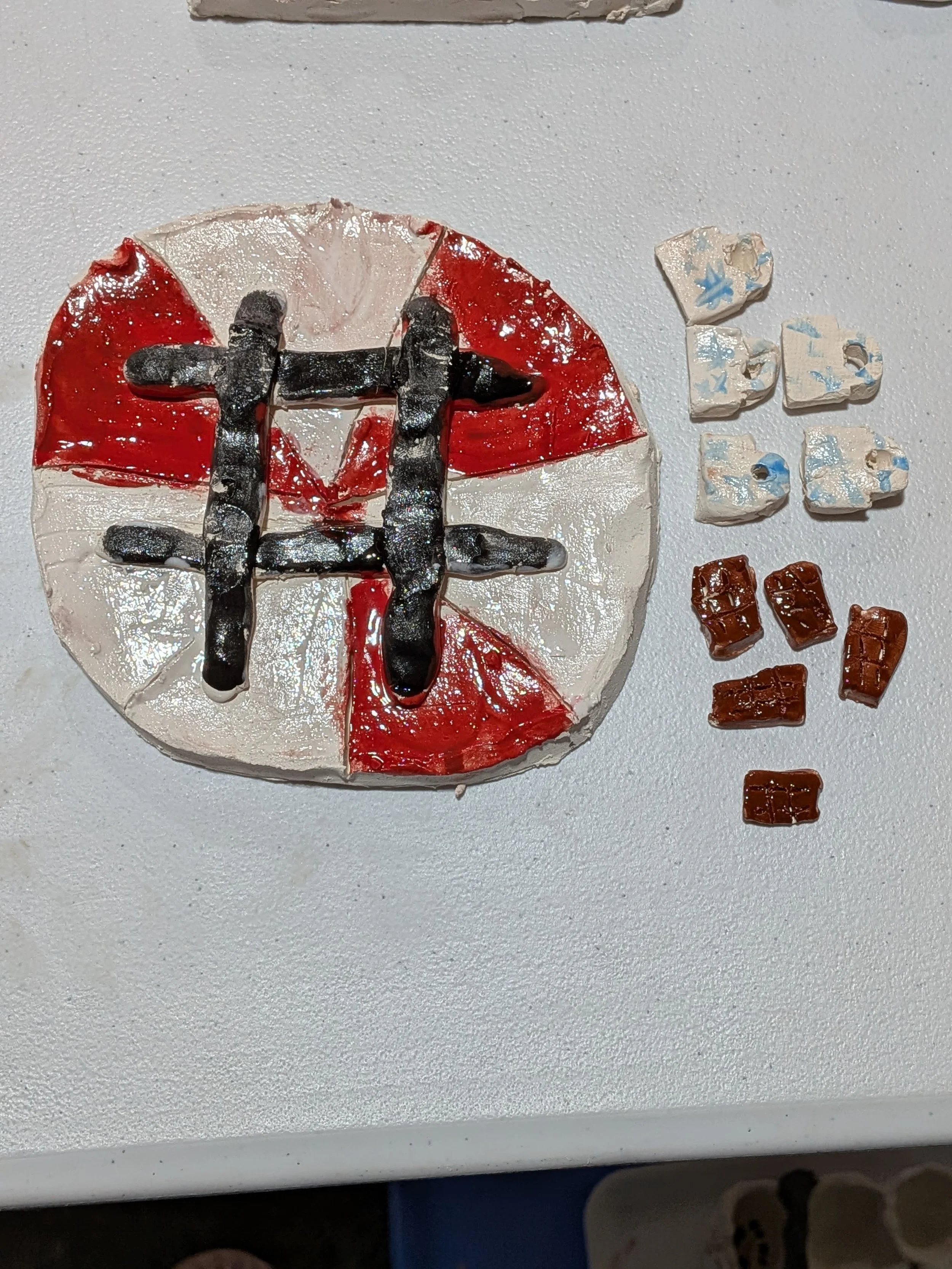 A cake decorated with red, white, and black icing resembling the England flag with a black cross on top. To the right of the cake are small candies in white, blue, and brown colors, resembling chocolates or gumdrops.