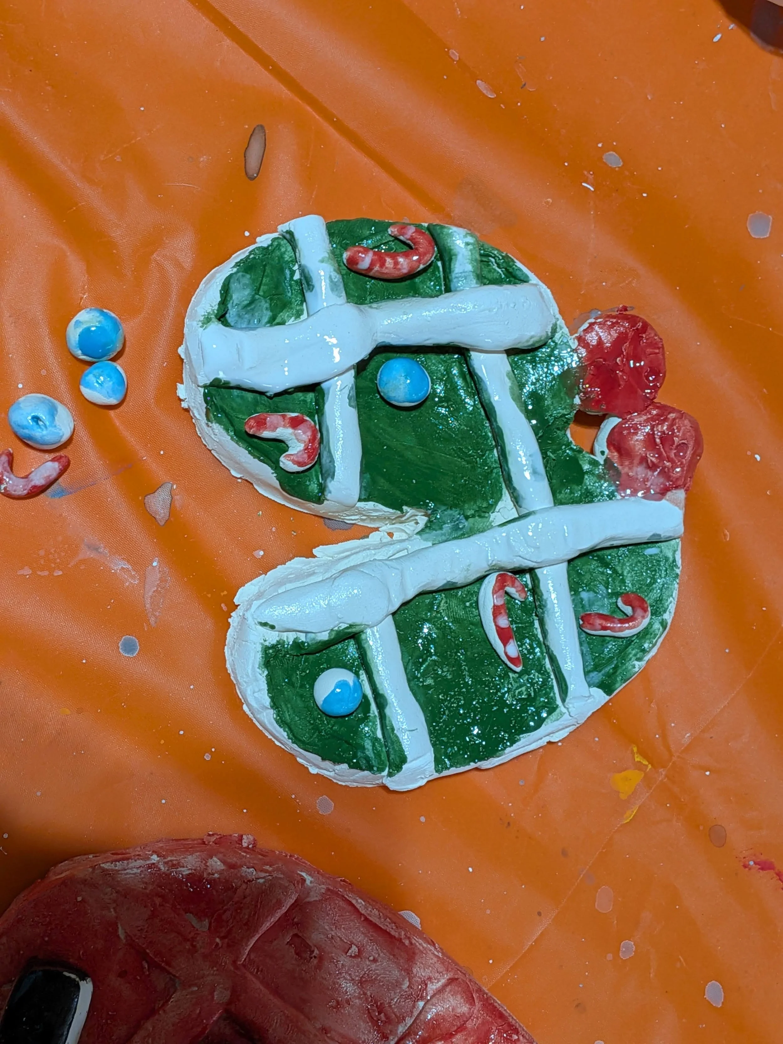 Decorative Christmas-themed cake with green frosting, white icing, red and blue candy decorations, placed on an orange surface.