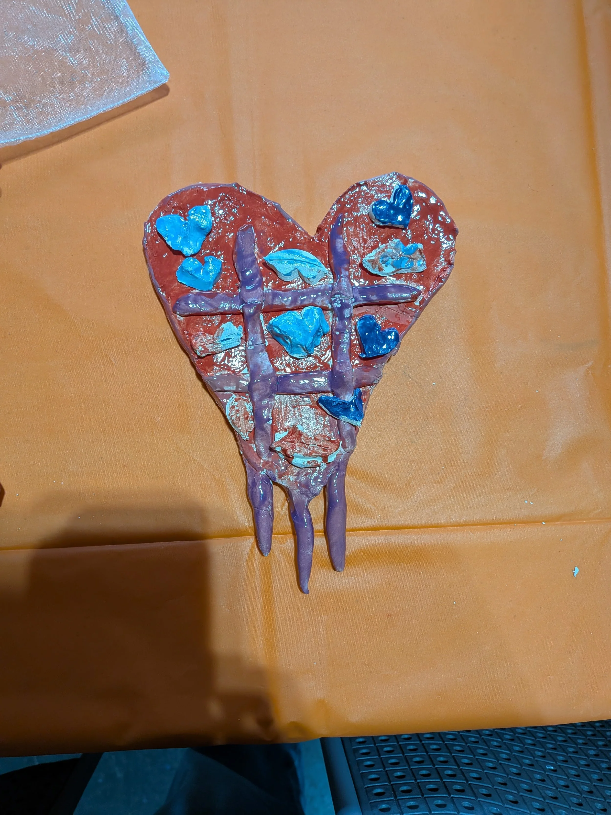 Heart-shaped craft with blue and purple stickers on an orange table.