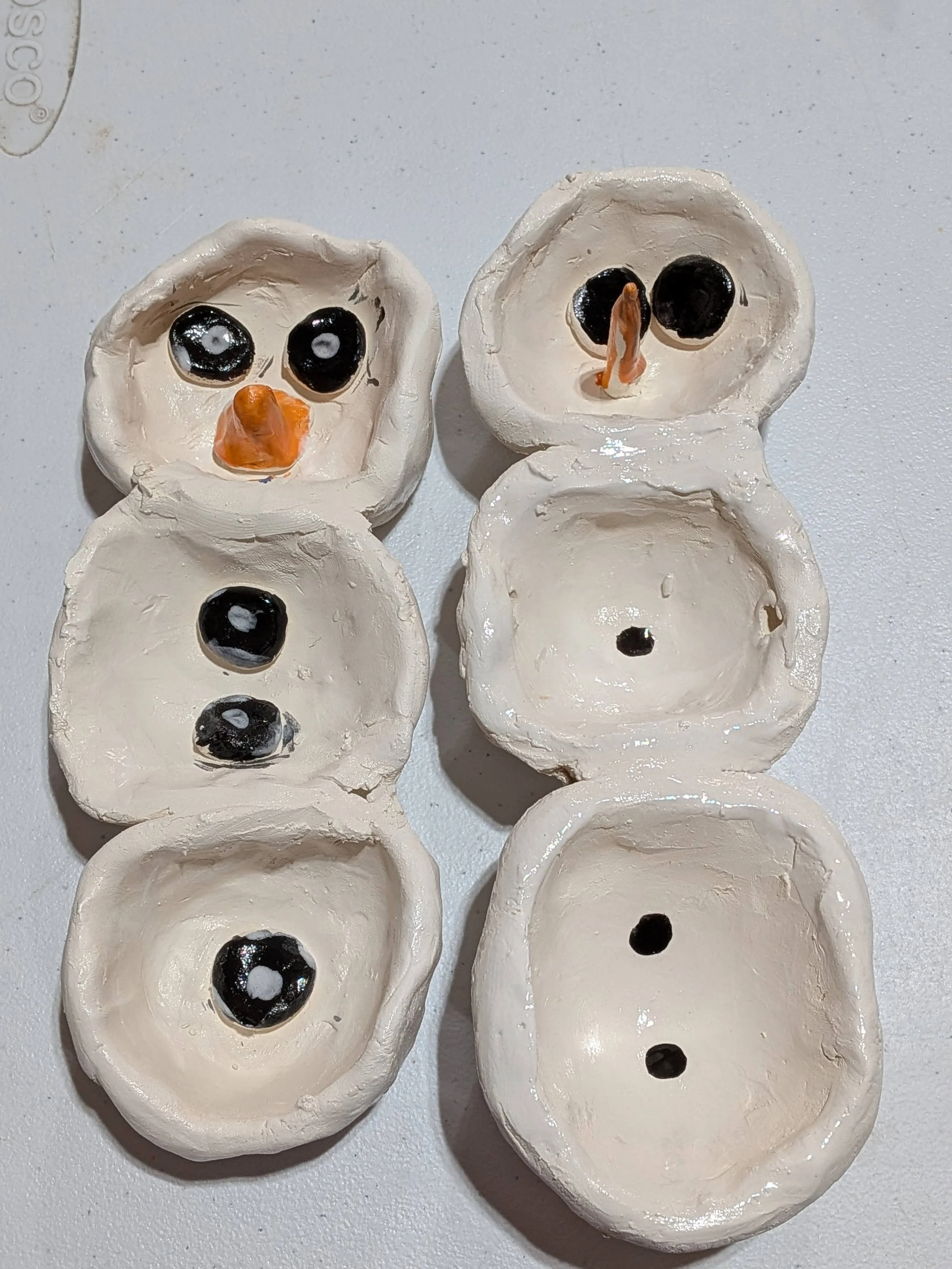 Handmade ceramic egg cartons with painted black olives and orange carrot pieces, some with faces and eyes.