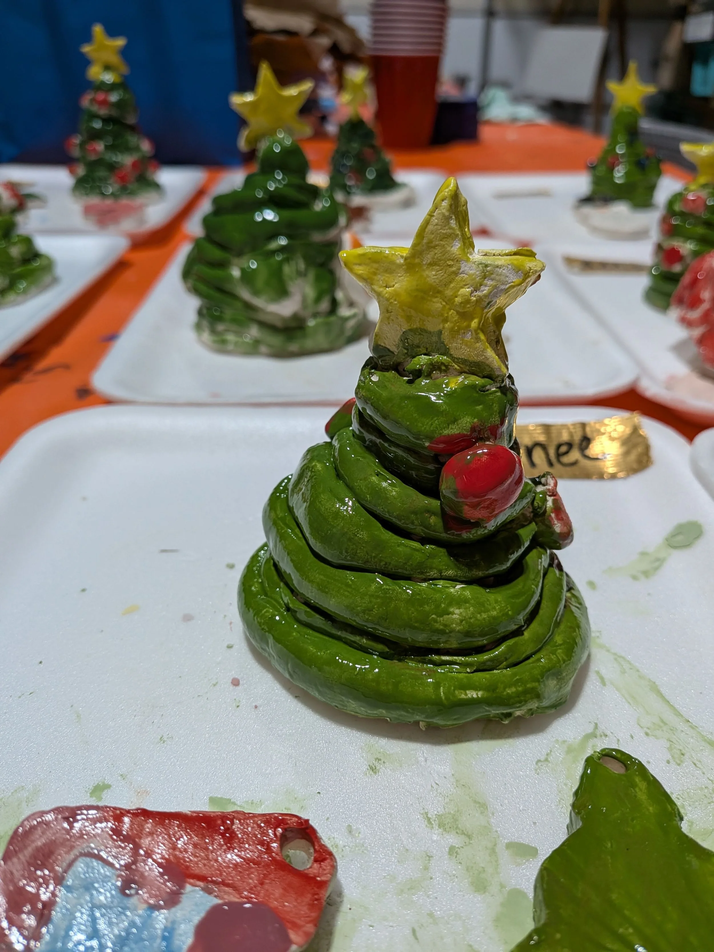 A Christmas tree shaped pastry decorated with green icing, a yellow star on top, and a small red ornament, displayed on a white tray.
