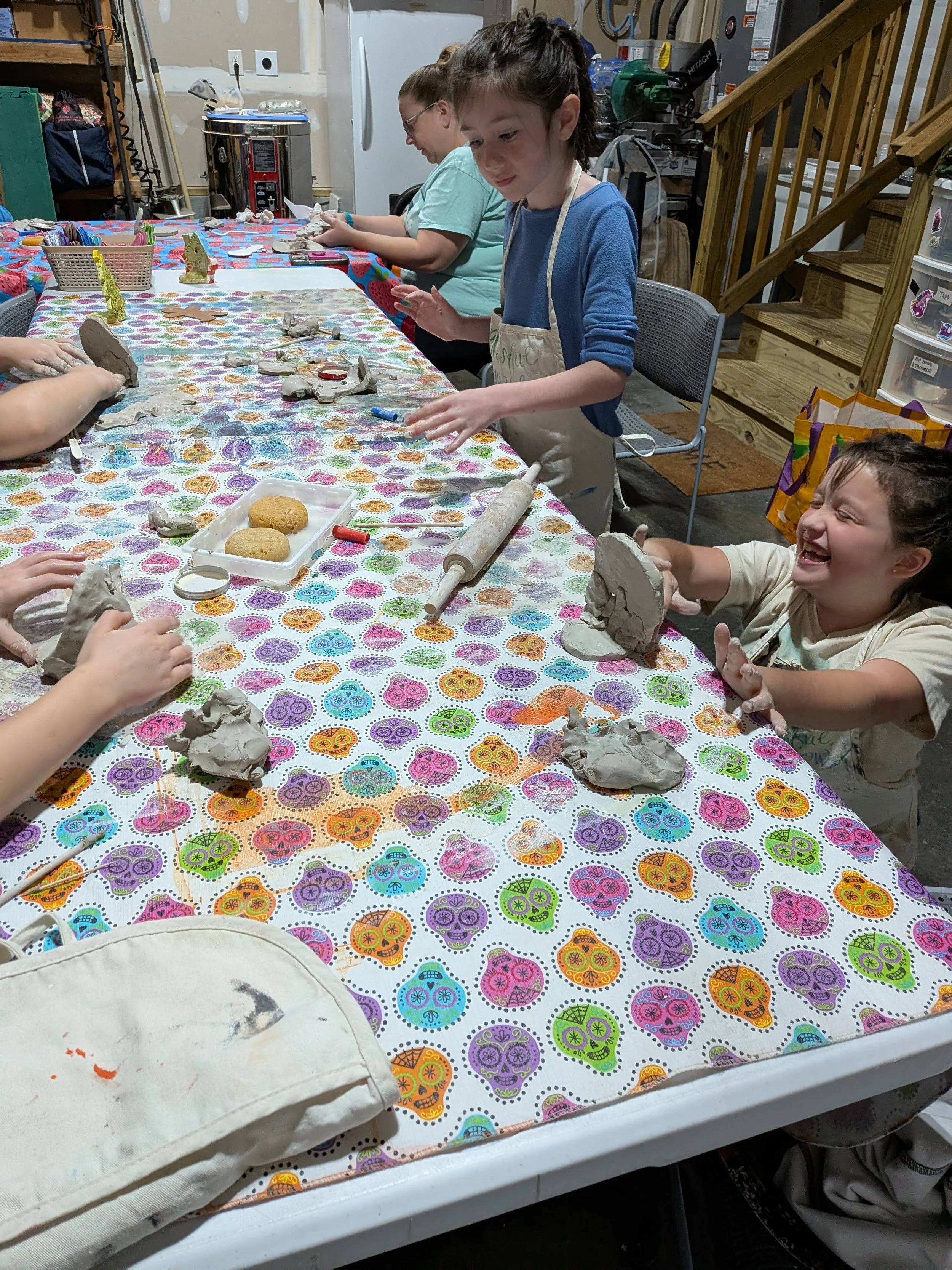 Children making clay sculptures around a colorful table in a garage workshop.