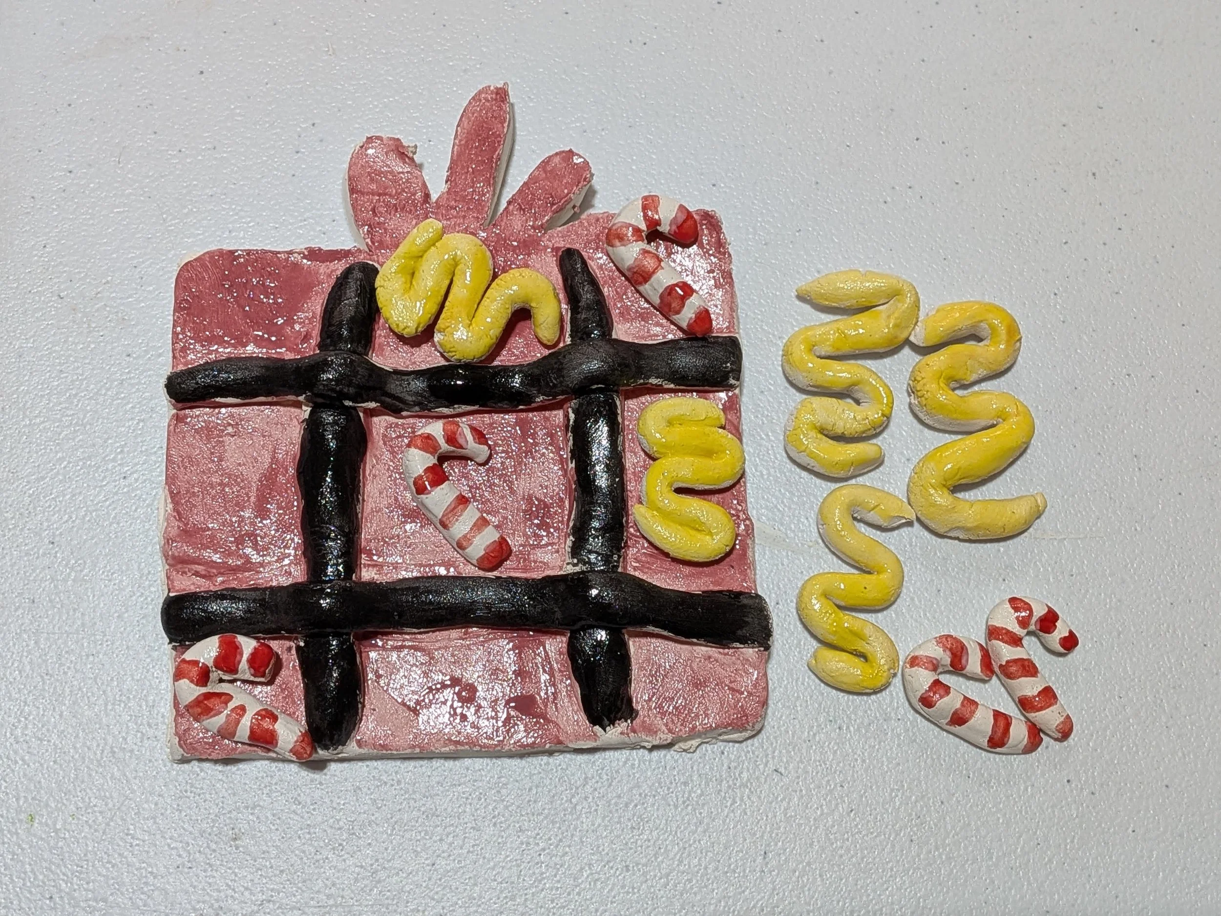 Decorative cookie designed to look like a wrapped present with candy canes and curly yellow and black lines on top, placed on a white surface.