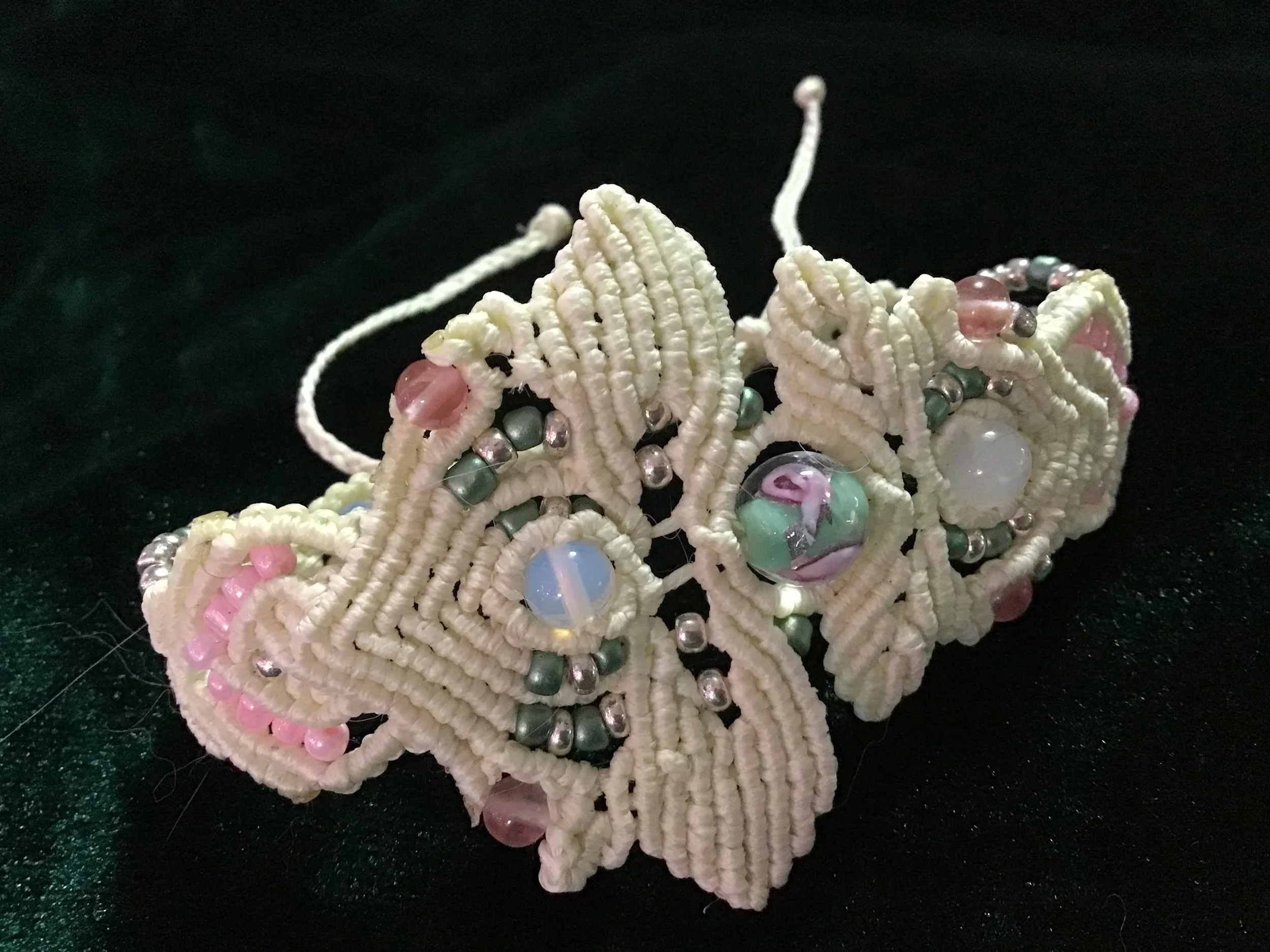 Beaded headpiece with cream-colored embroidery, pink, green, blue, and metallic beads, decorated with fabric and bead details, on a black background.