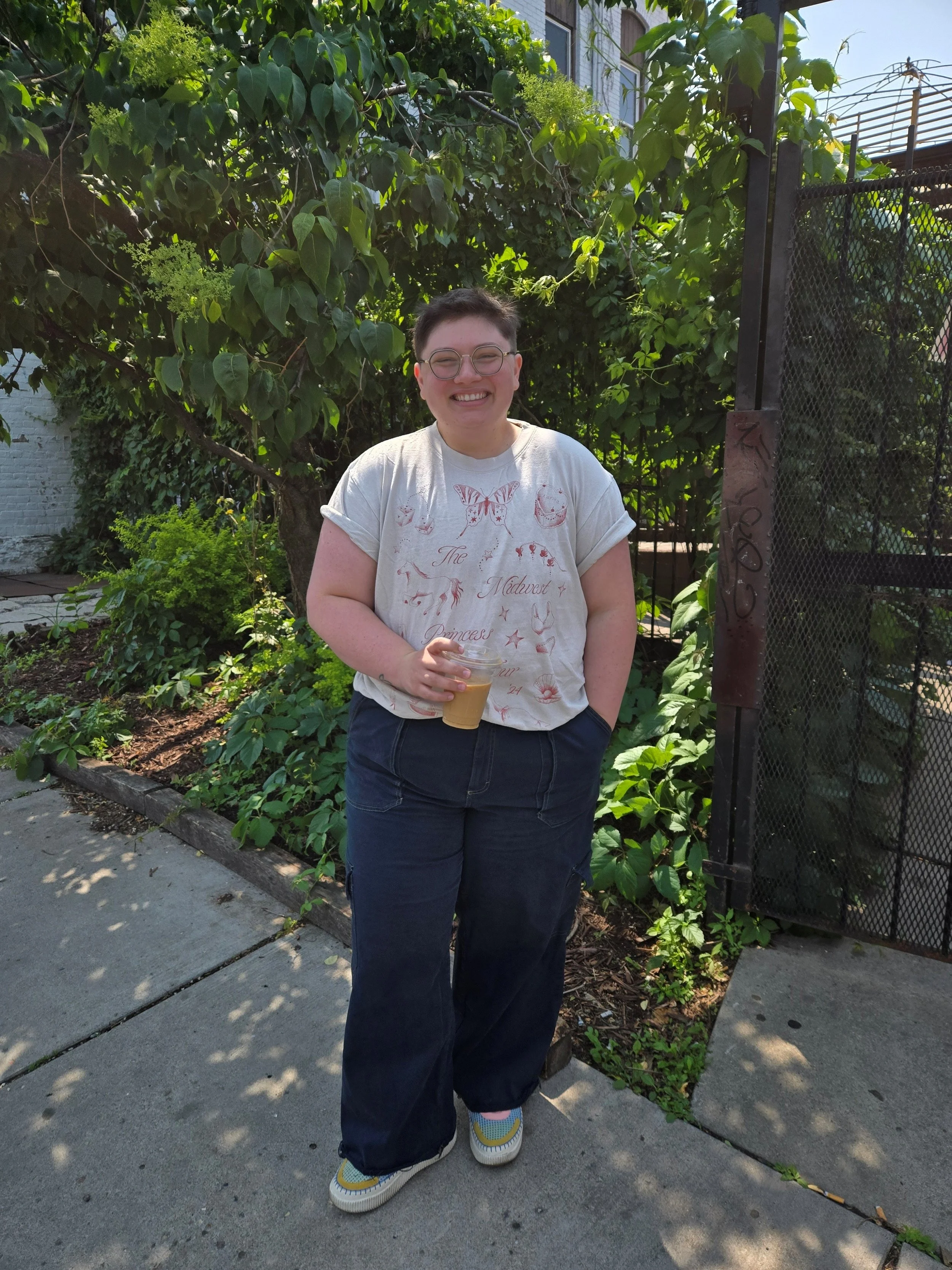 Dr. Kyla Leonard, a white fat queer person standing outside in casual clothes holding coffee