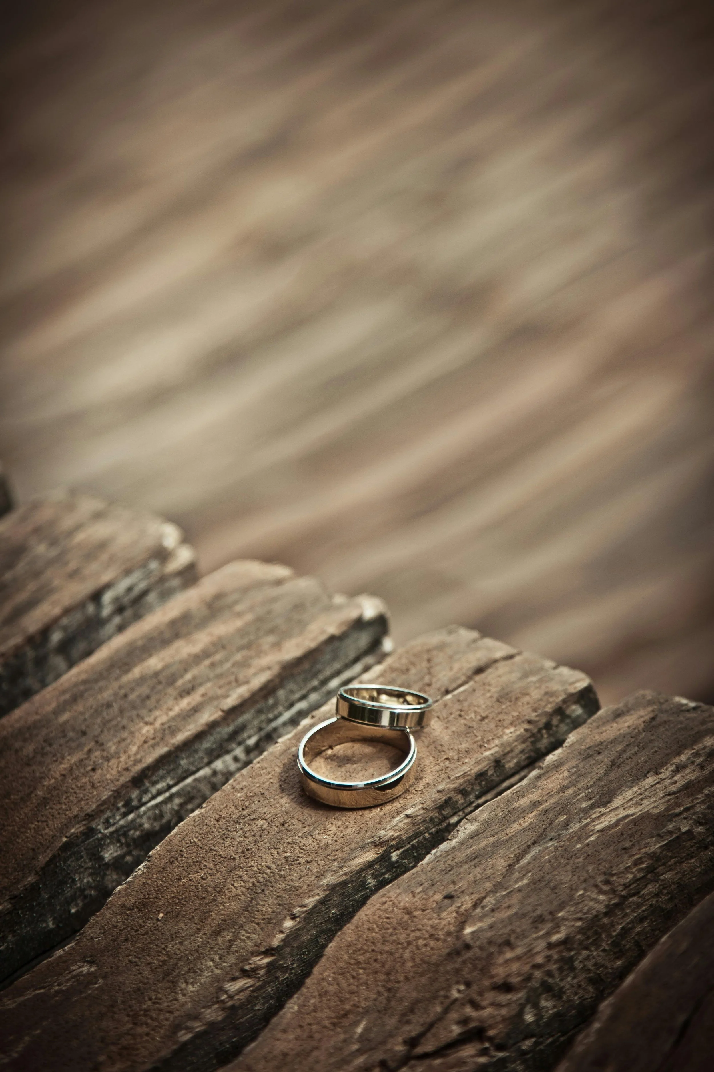 Two silver rings placed on a weathered wooden surface with blurred water in the background.