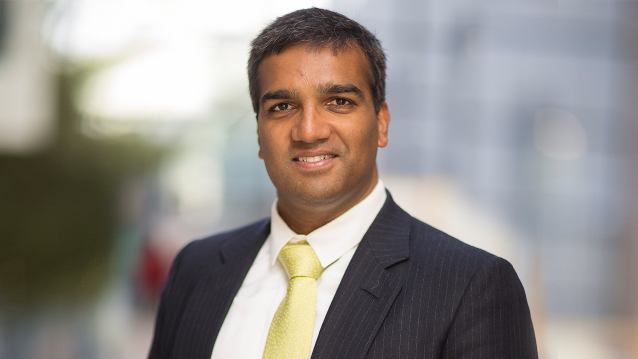 Professional man in suit and yellow tie standing outdoors with blurred background.