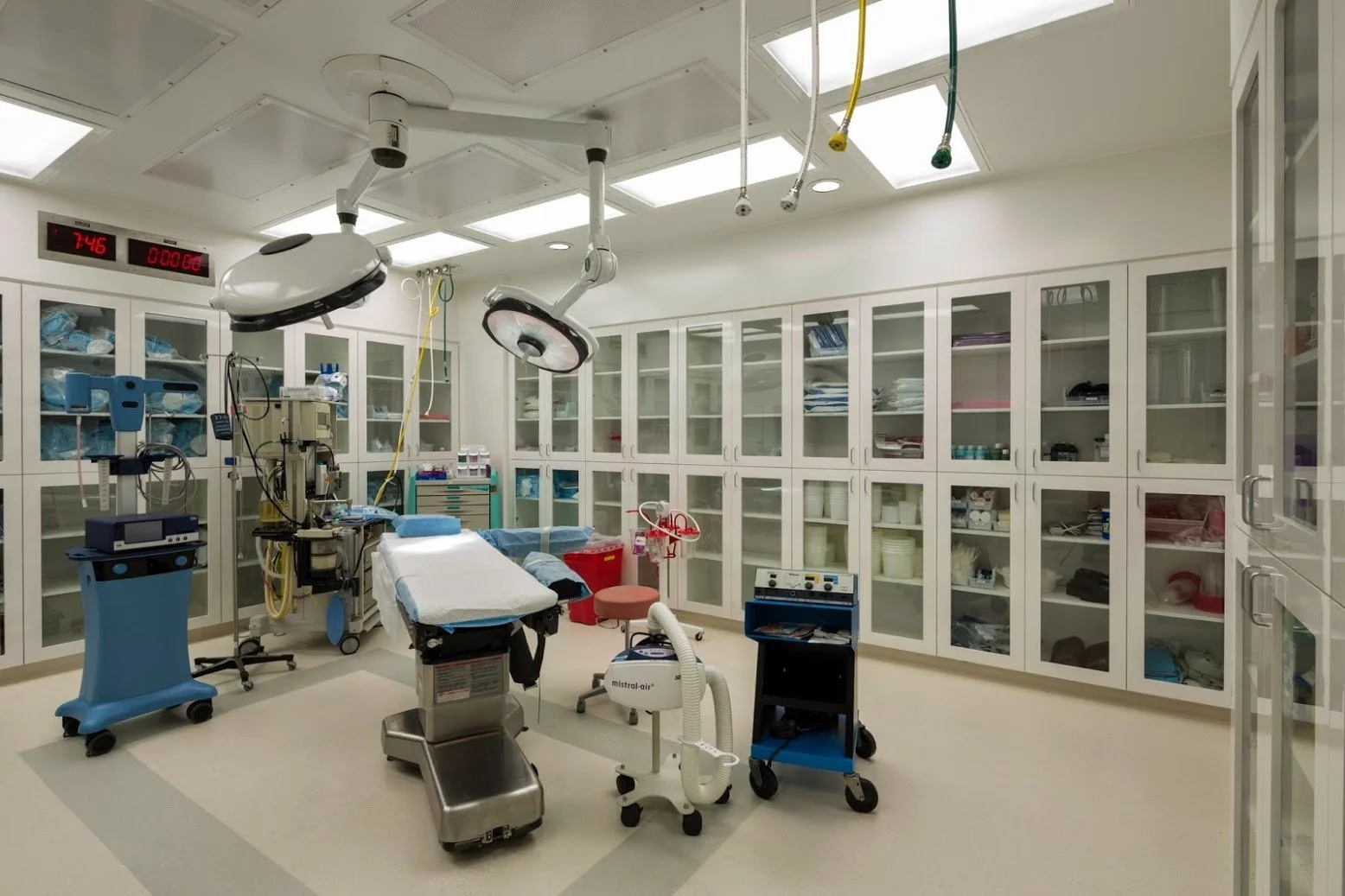 A clean, well-organized hospital operating room with surgical lights, medical equipment, and cabinets filled with supplies.
