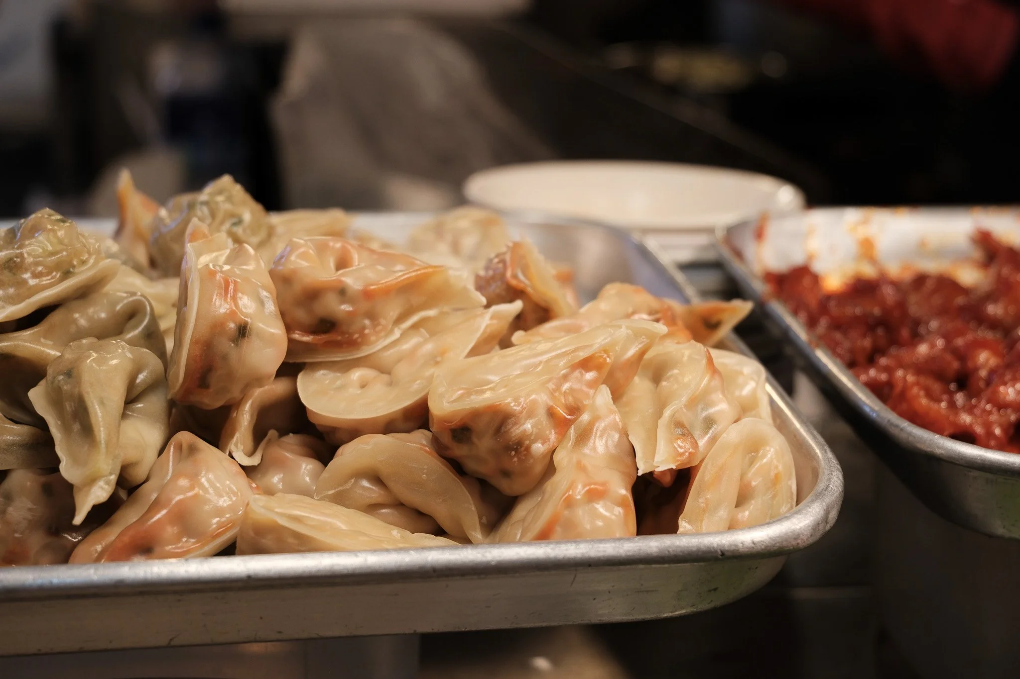 Dampfende chinesische Teigtaschen, bekannt als Jiaozi, auf einem Blech, mit einer Tomatensauce im Hintergrund
