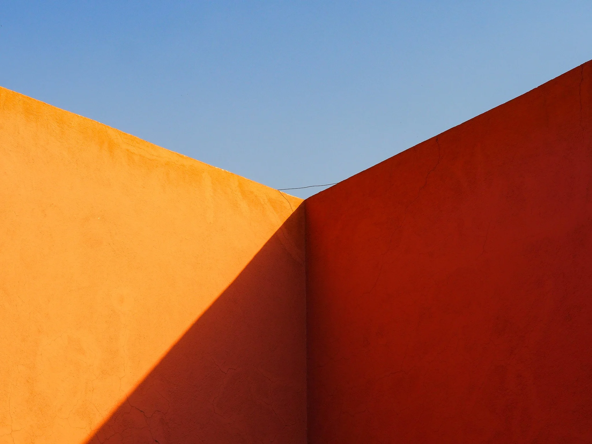 Bunte farbige Wände in Orange und Rot gegen blauen Himmel, mit Schatten und leichten Rissen in der Oberfläche.