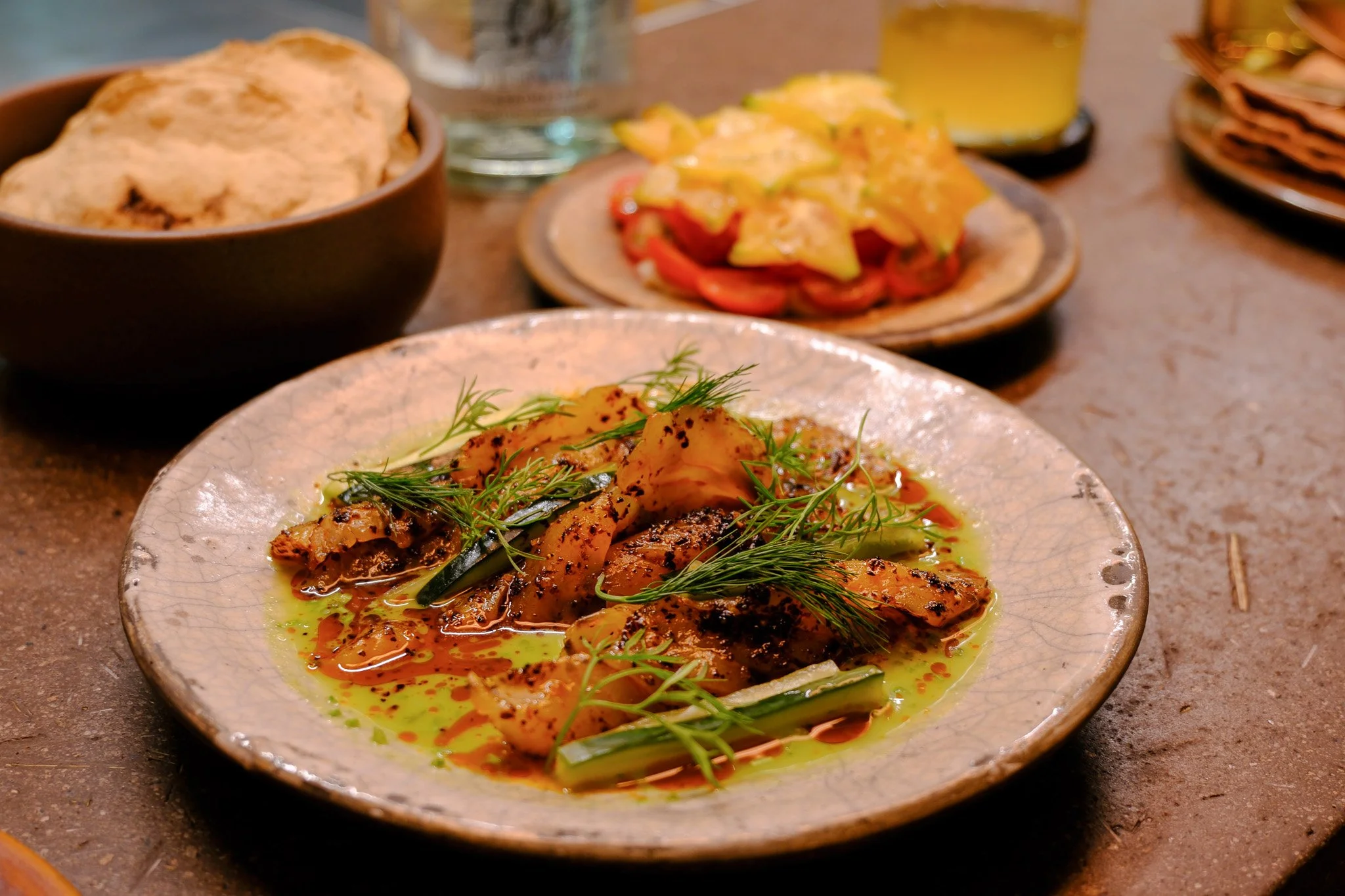 Verschiedene italienische Gerichte auf Tellern, darunter gegrilltes Fleisch mit Kräutern und Öl, Pasta mit Tomaten und Sauce, Brot in einer Schüssel, und Getränke auf Holztisch.