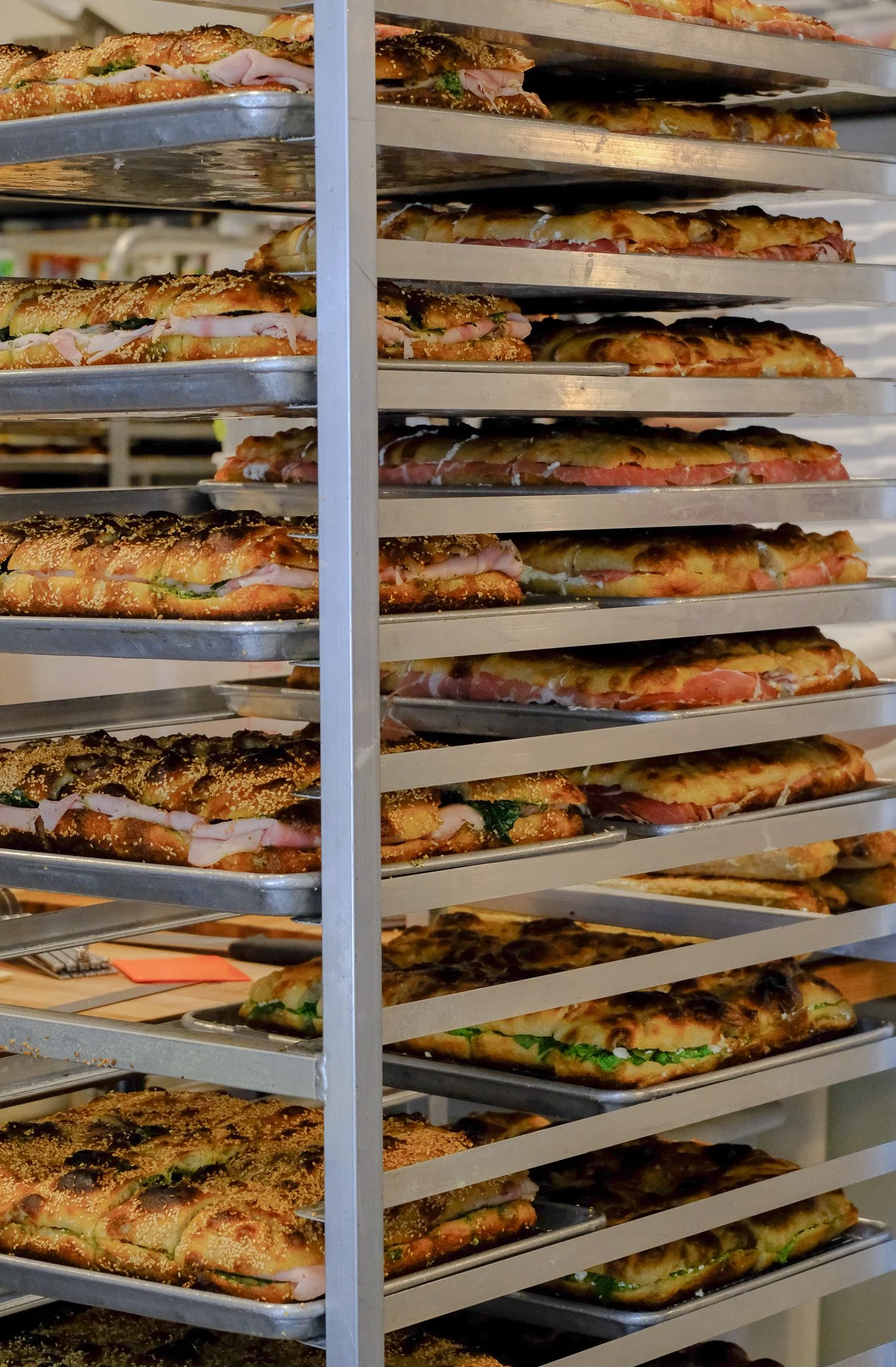 Mehrere kalziumreiche Pizzastücke auf Metalblechen gestapelt, mit verschiedenen Belägen wie Fleisch, Käse und Gemüse.