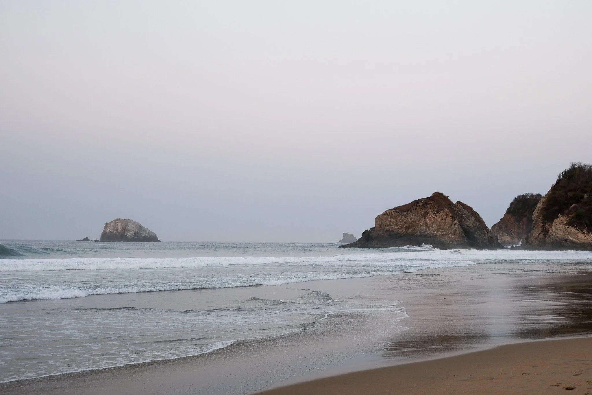 Strand mit Felsen im Meer bei bewölktem Himmel