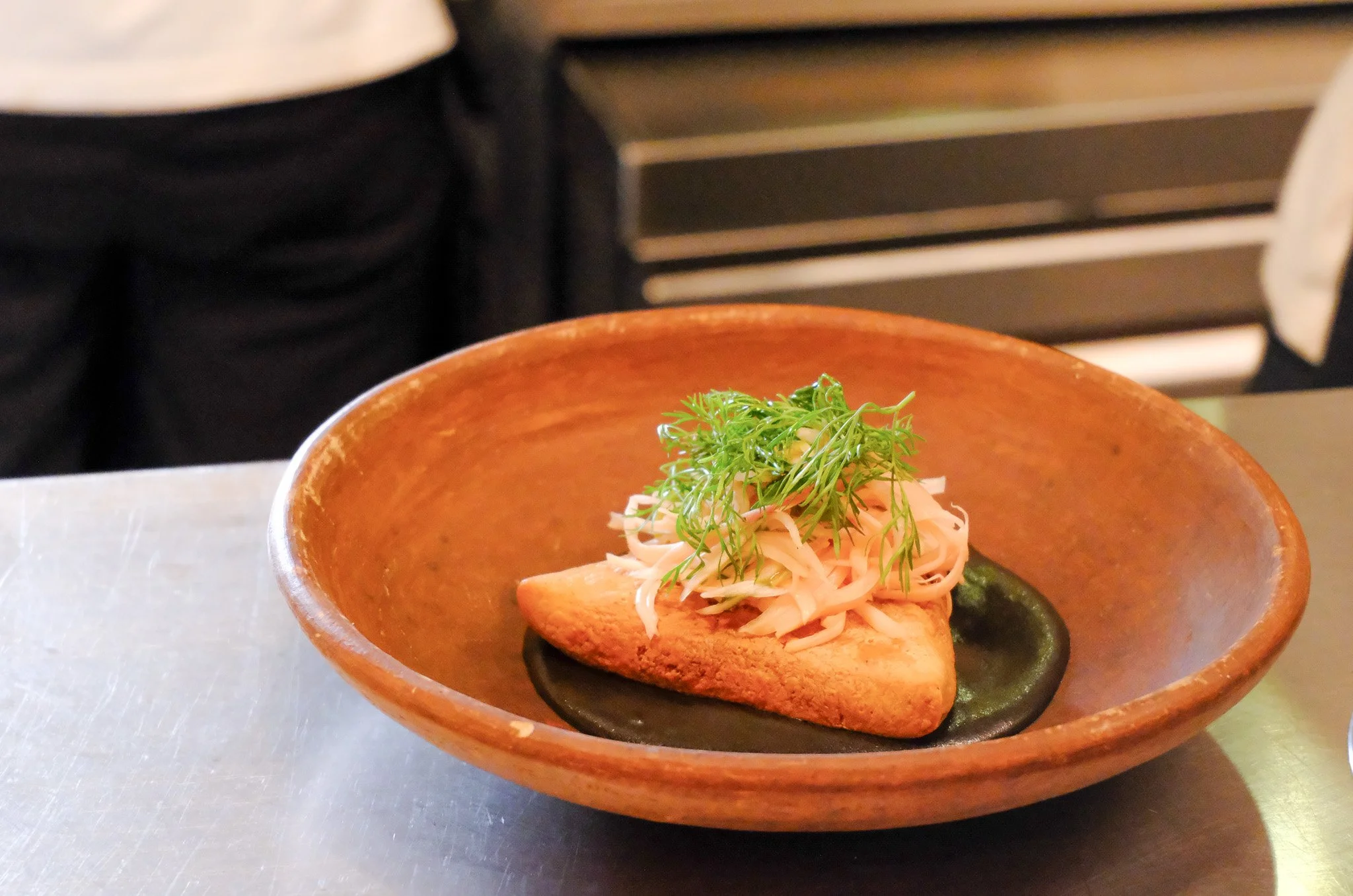 Gedünsteter Fisch mit Salat auf einem schwarzen Teller in einer braunen Schüssel