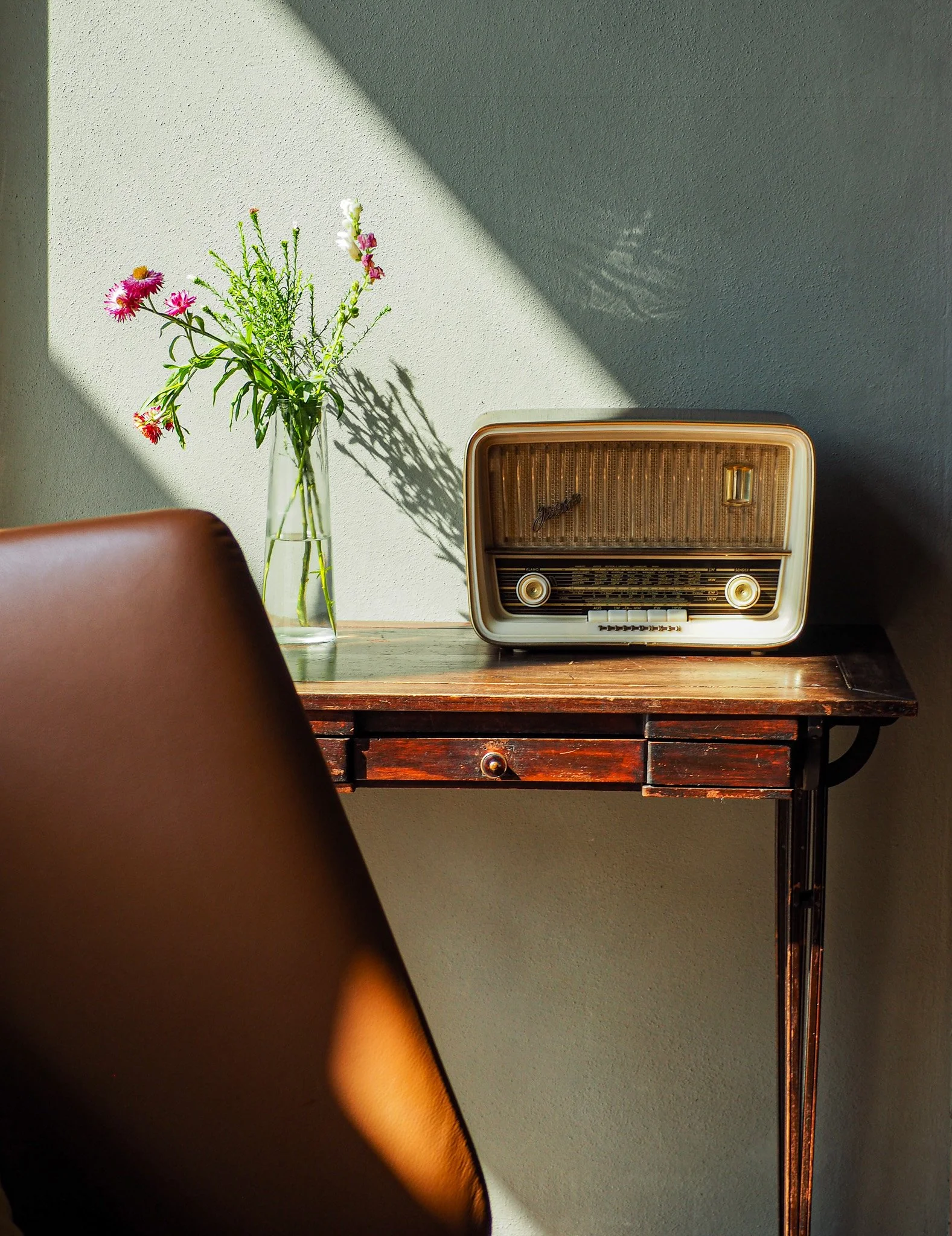 Vintage-Radiowecker und eine Vase mit Blumen auf einem Holzschreibtisch, Sonnenlicht und Schatten an der Wand.