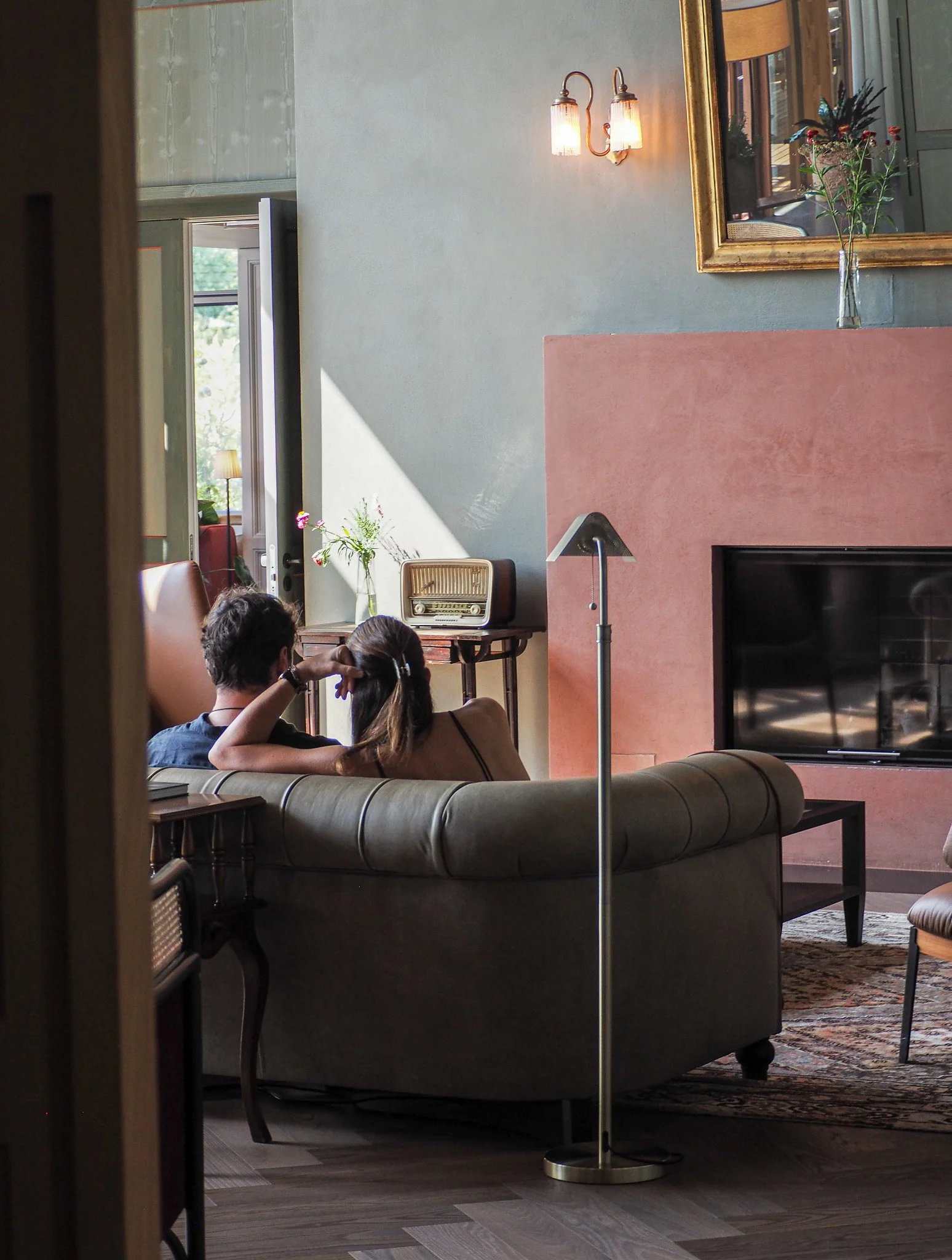 Zwei Menschen sitzen auf einem Sofa in einem gemütlichen Wohnzimmer, das mit einem Kamin, einem Kamin-Ofen, einer Stehlampe und einem Fernseher ausgestattet ist.