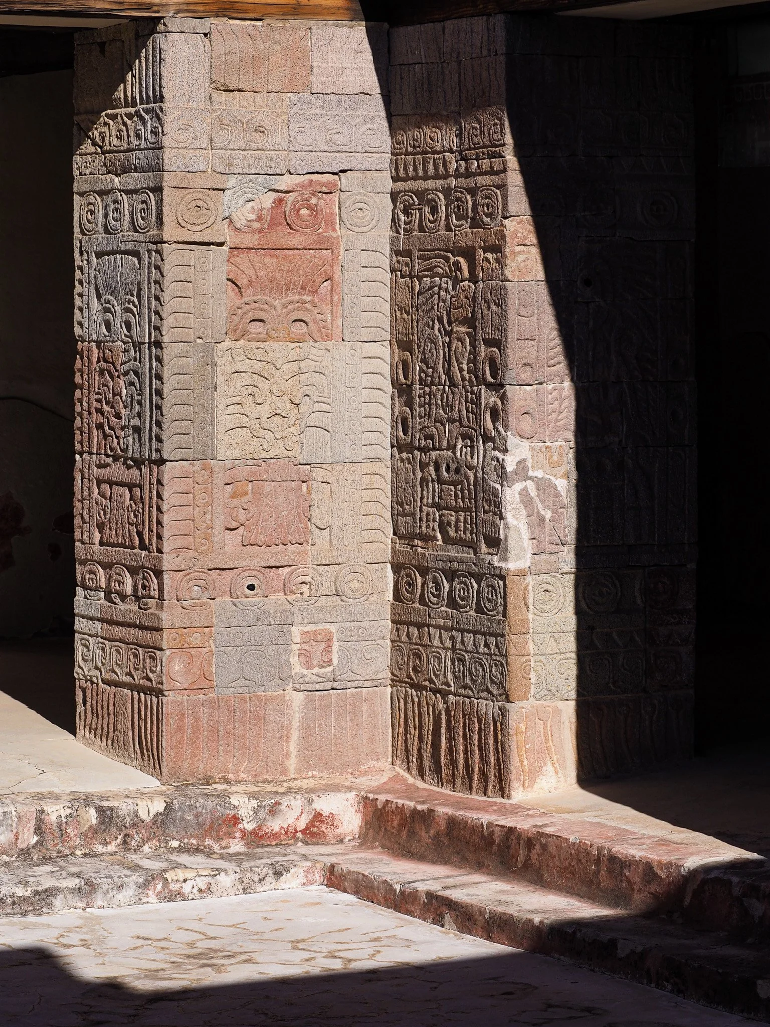 Steinmauer mit hieroglyphenartigen Gravuren, teilweise im Schatten, am Boden Steinplatten, wahrscheinlich eine antike Tempelwand in Mexiko.