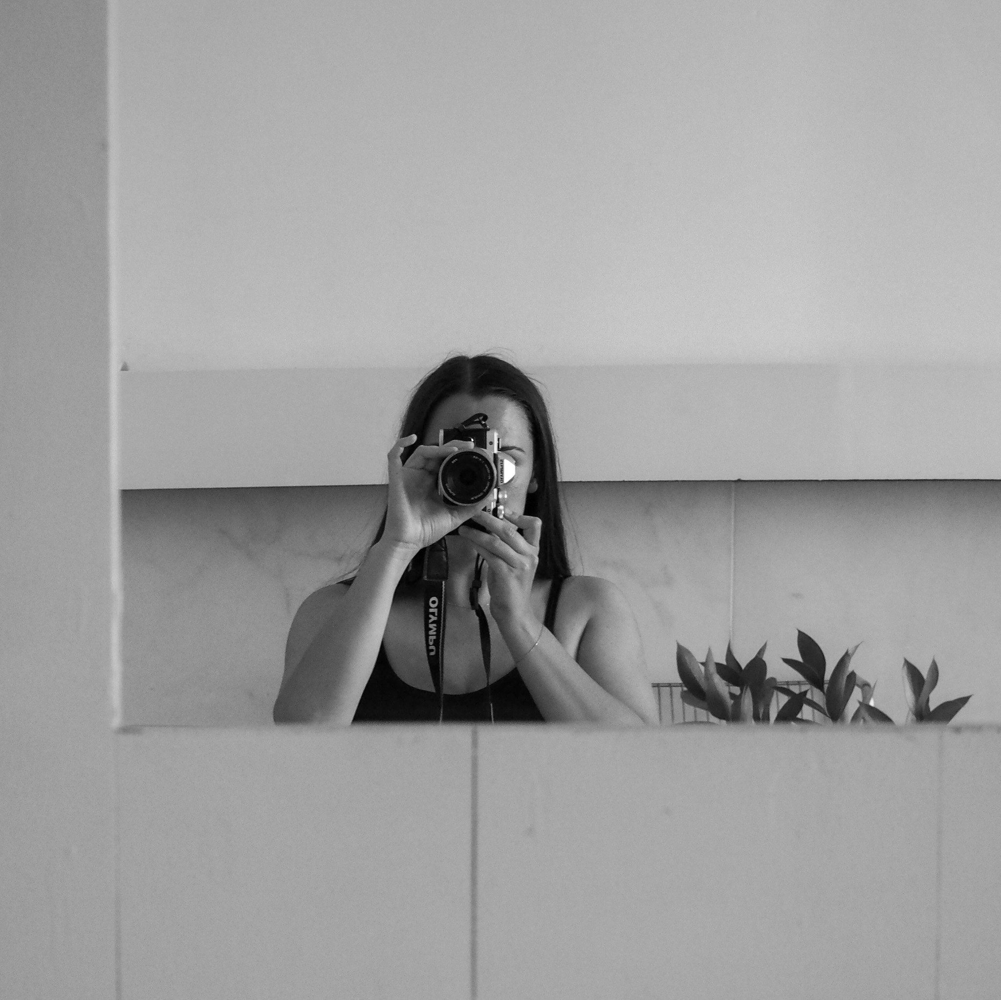 Eine Frau fotografiert sich selbst in einem Spiegel; das Bild ist schwarz-weiß.