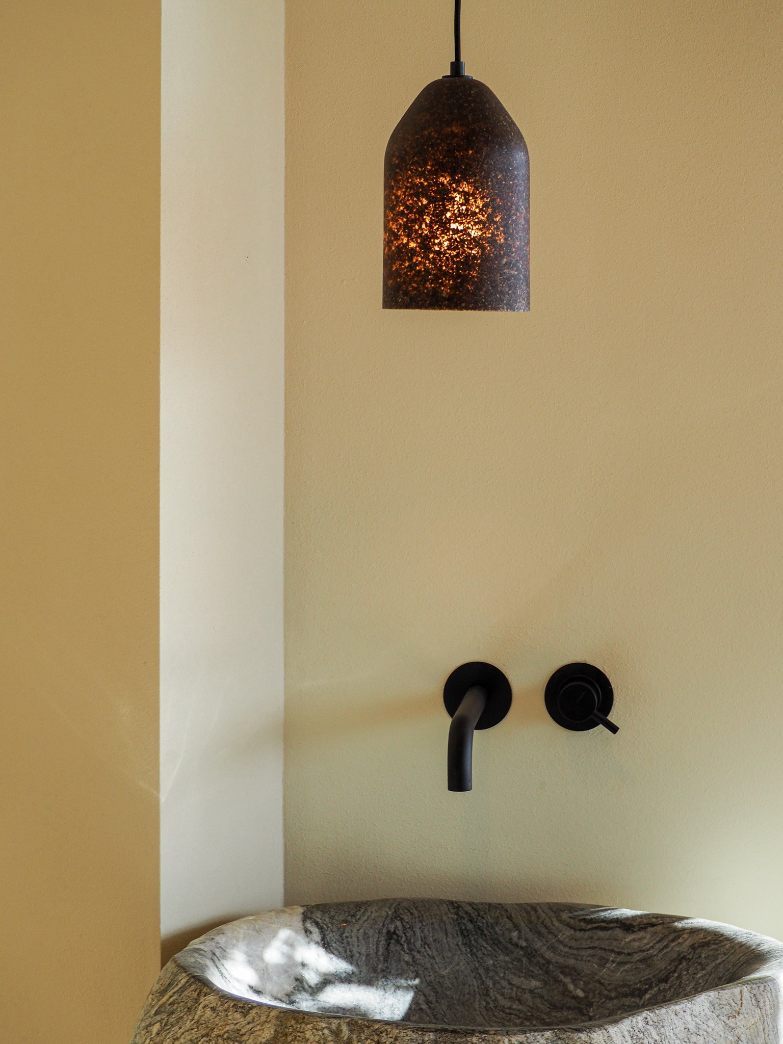 Waschbecken mit schwarzer Wasserhahn und schwarzem Licht hanging in einer gelben Wand