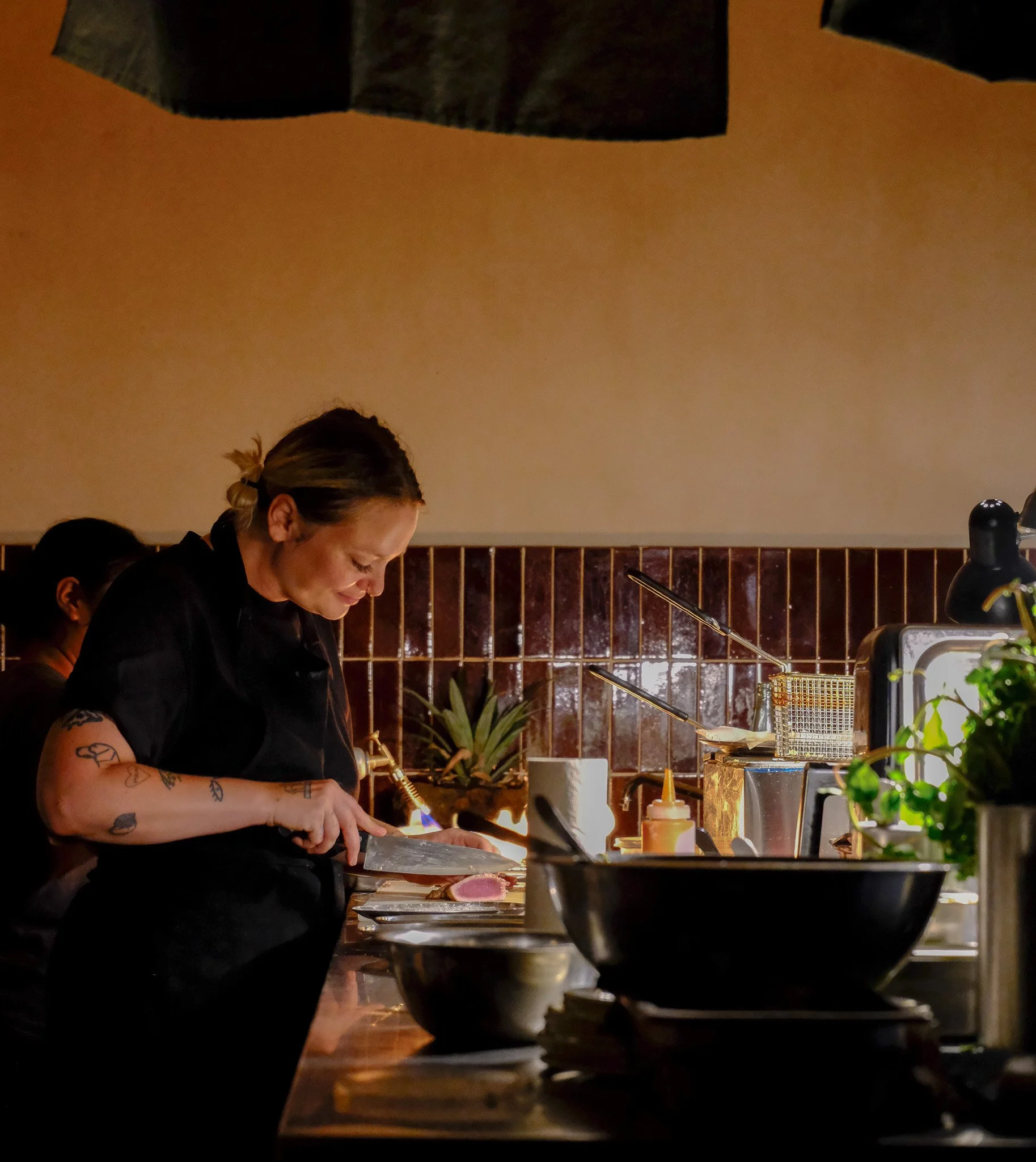 Kochin in einer dunklen Küche beim Schneiden eines Fleischstücks.