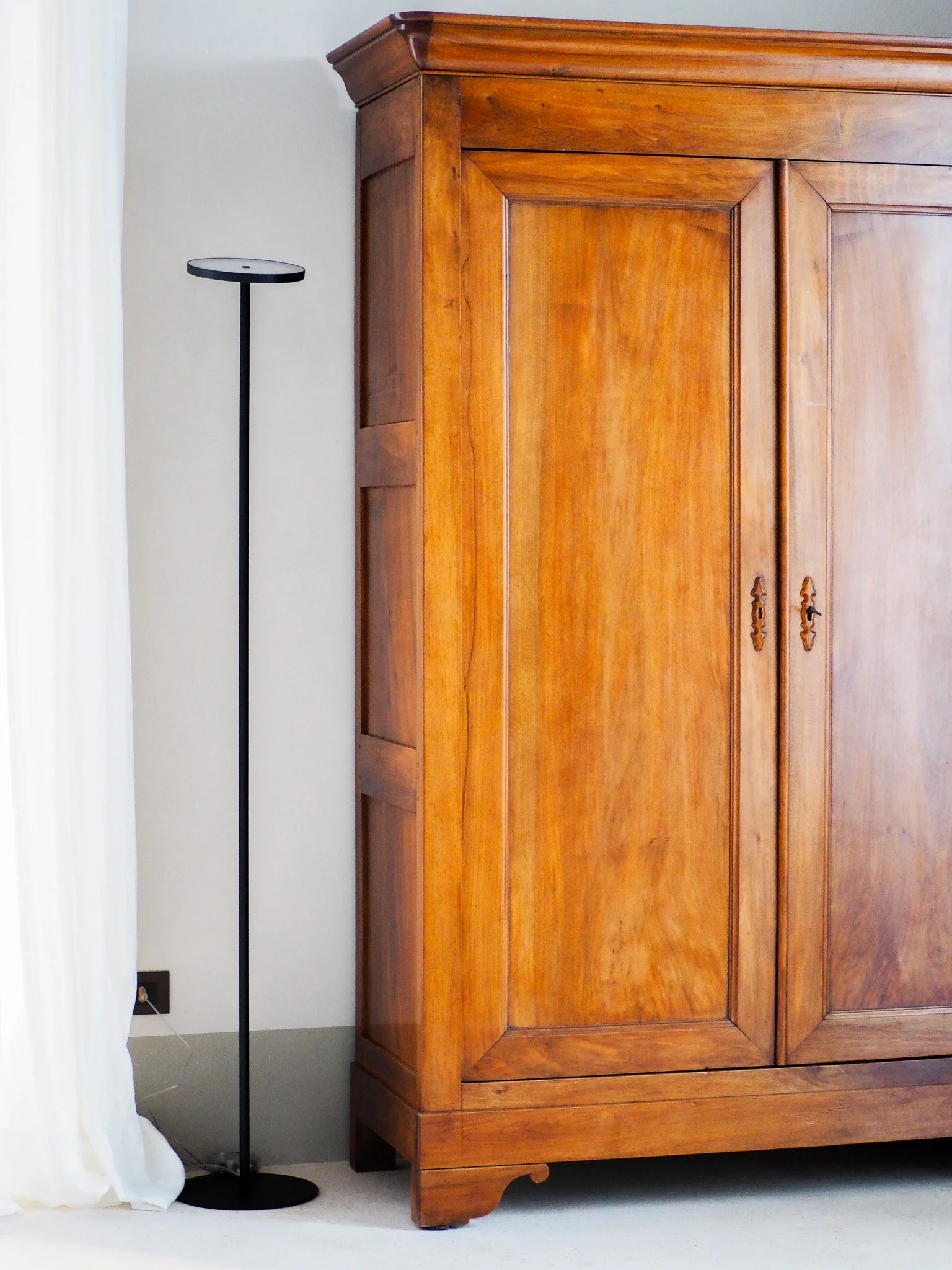 Ein großes, braunes Holzschrank steht neben einem schwarzen Stehlampen in einem Zimmer.