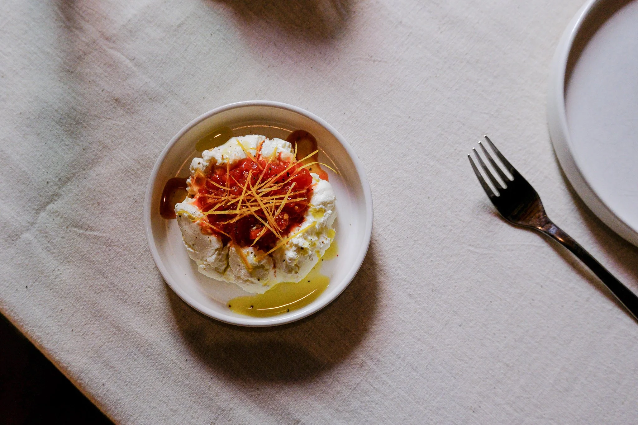 Ein Teller mit Mozzarella-Käse, verziert mit Tomatensauce, Olivenöl und gehacktem Gemüse, auf einem weißen Tuch. Ein Messer und eine Gabel liegen neben dem Teller.