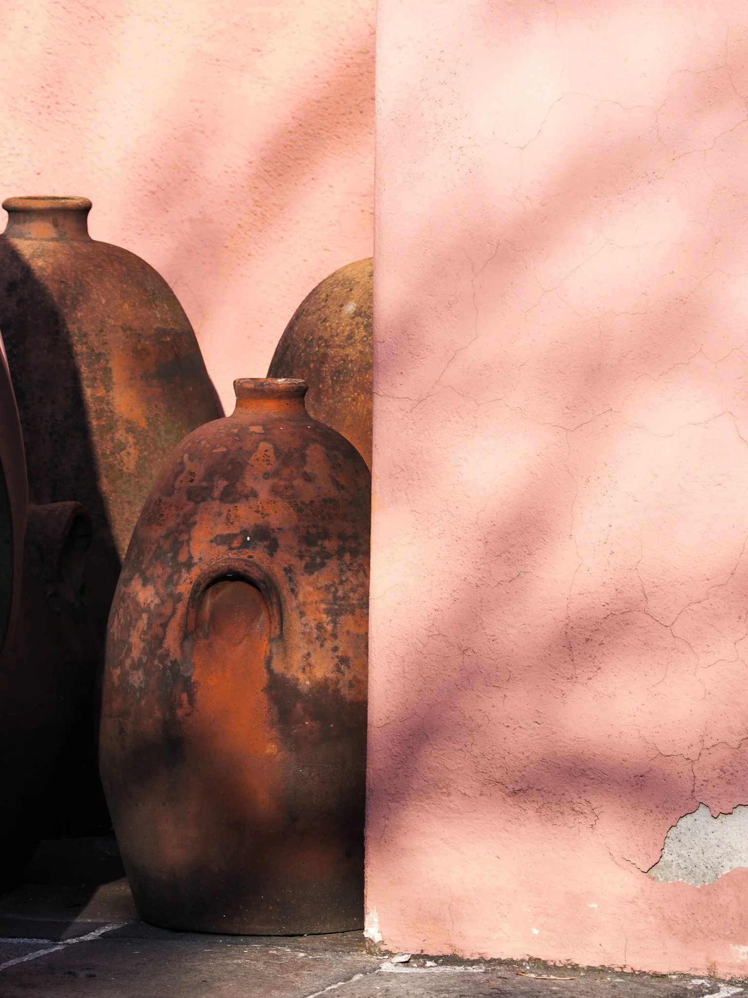 Alte, rustikale Tongefäße stehen an eine rosa verputzte Wand gelehnt.