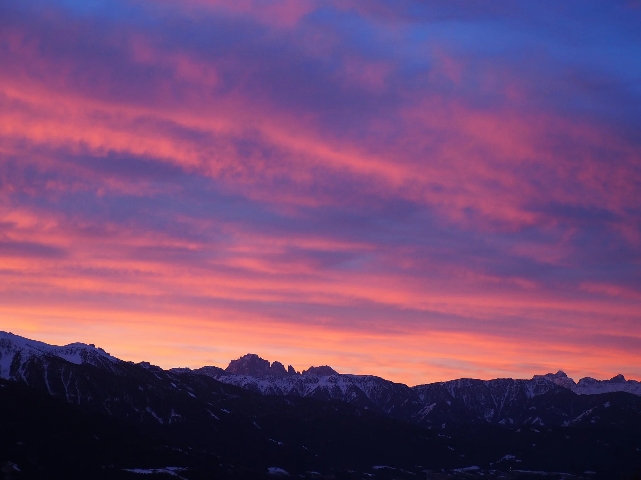 Berglandschaft bei Sonnenuntergang mit farbigen Wolken am Himmel.