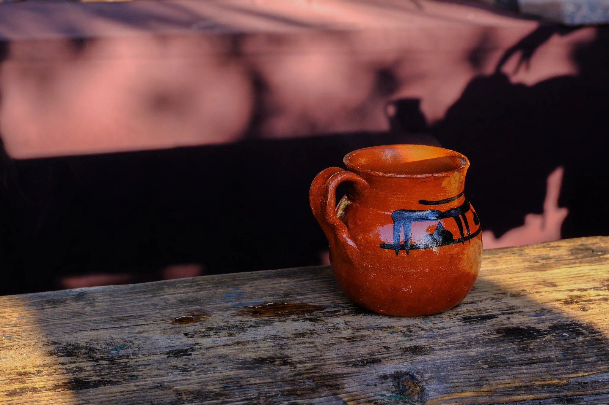 Eine kleine terrakottafarbene Teekanne mit schwarzer und blauer Verzierung auf einem alten Holztisch.