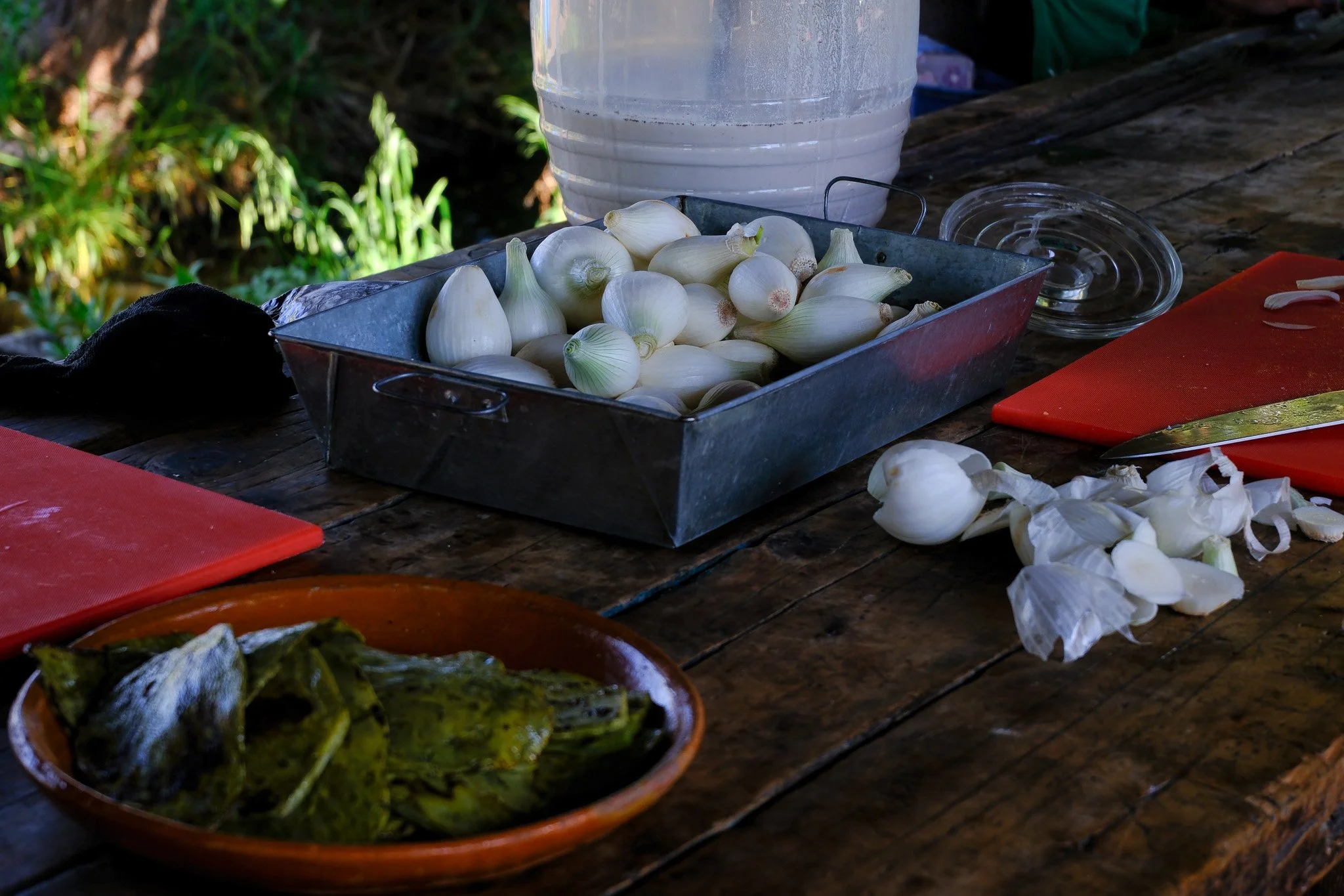 Ein Tisch mit Knoblauchzehen, Kürbissen und Küchenutensilien, darunter ein Messer, Schneidbretter, ein Glas und eine Metallbox.