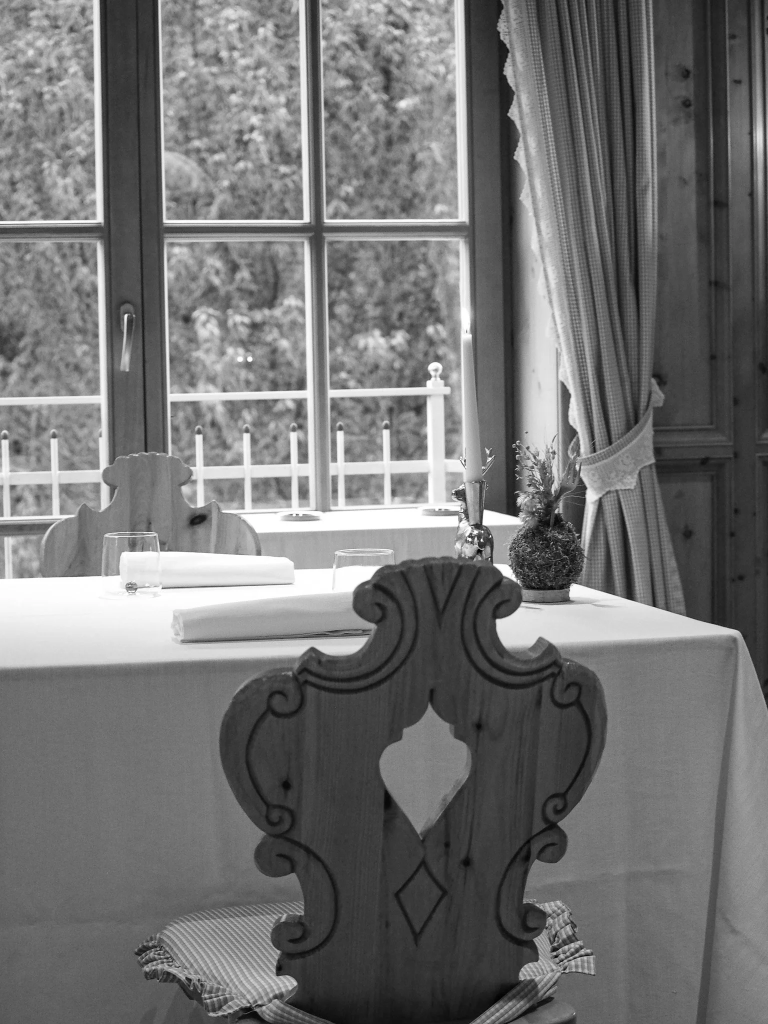 Ein gedeckter Tisch im Wohnzimmer mit Kerze, Besteck, Weingläser und eine Vase, vor einem großen Fenster mit Blick nach draußen.