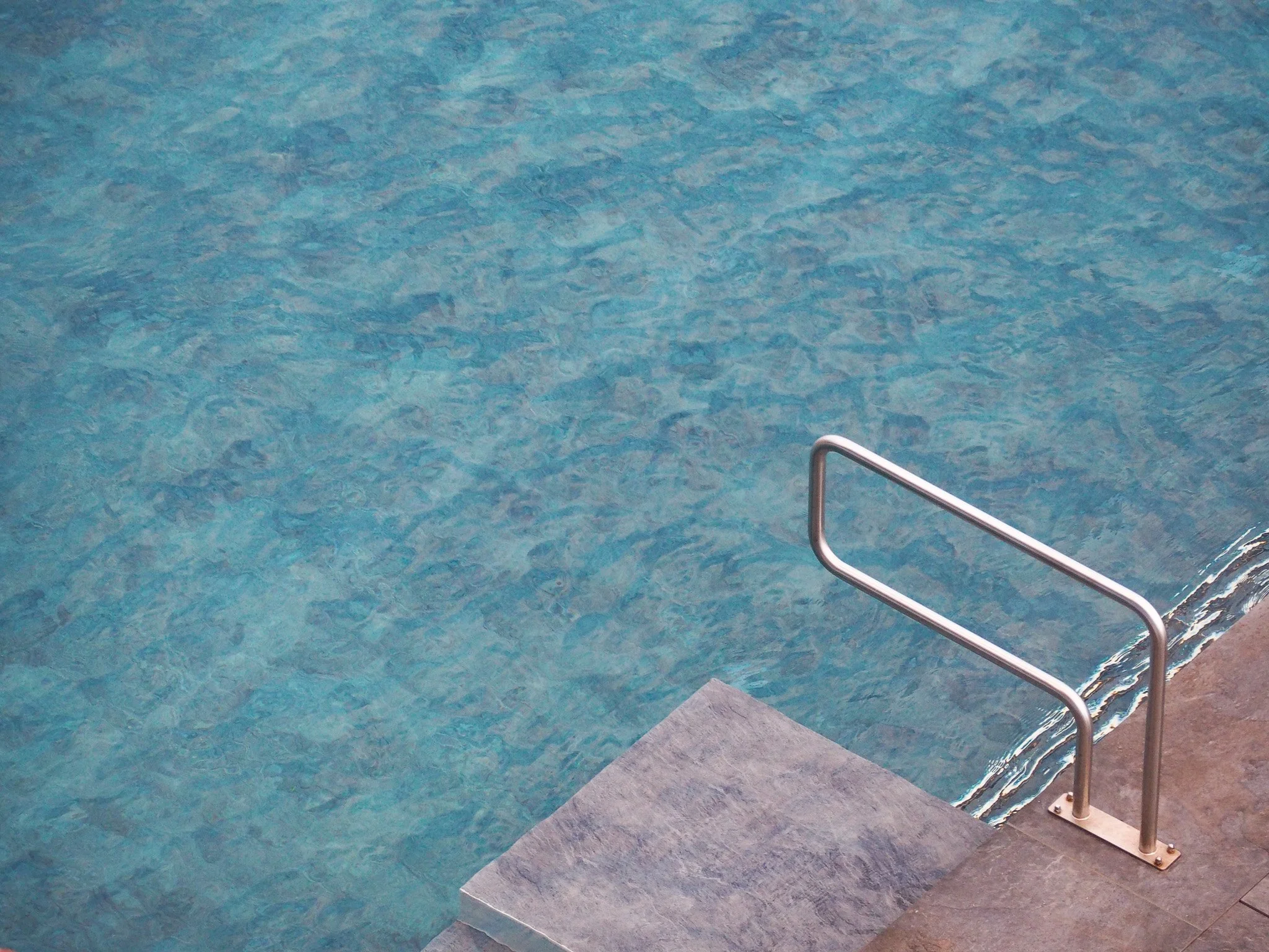 Schwimmbad mit Wasser, Metallgeländer und Steg aus Fliesen.