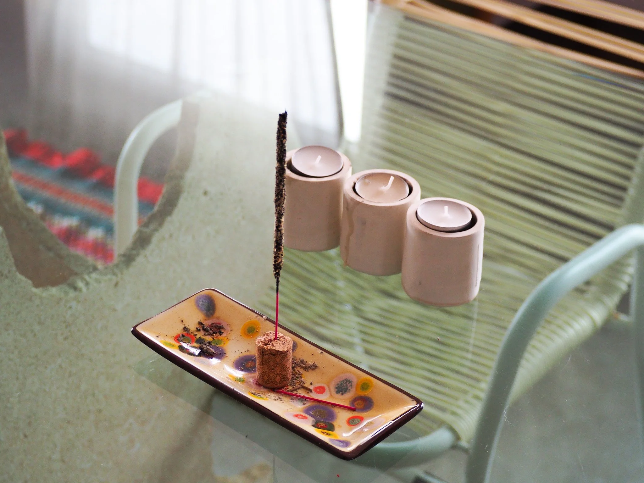 Kerze, eine feuerfeste Platte, drei Kerzen, ein Spiegel, eine Lamellen-Fensterläden, ein Rattansessel.