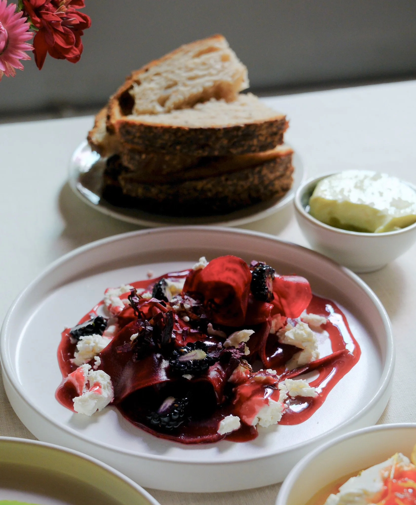 Büffet mit rotem Tafelspitz, Heidelbeeren, Rote Beete, Rucola, Feta auf weißem Teller, daneben Roggenbrot und Butter in kleinen Schalen.