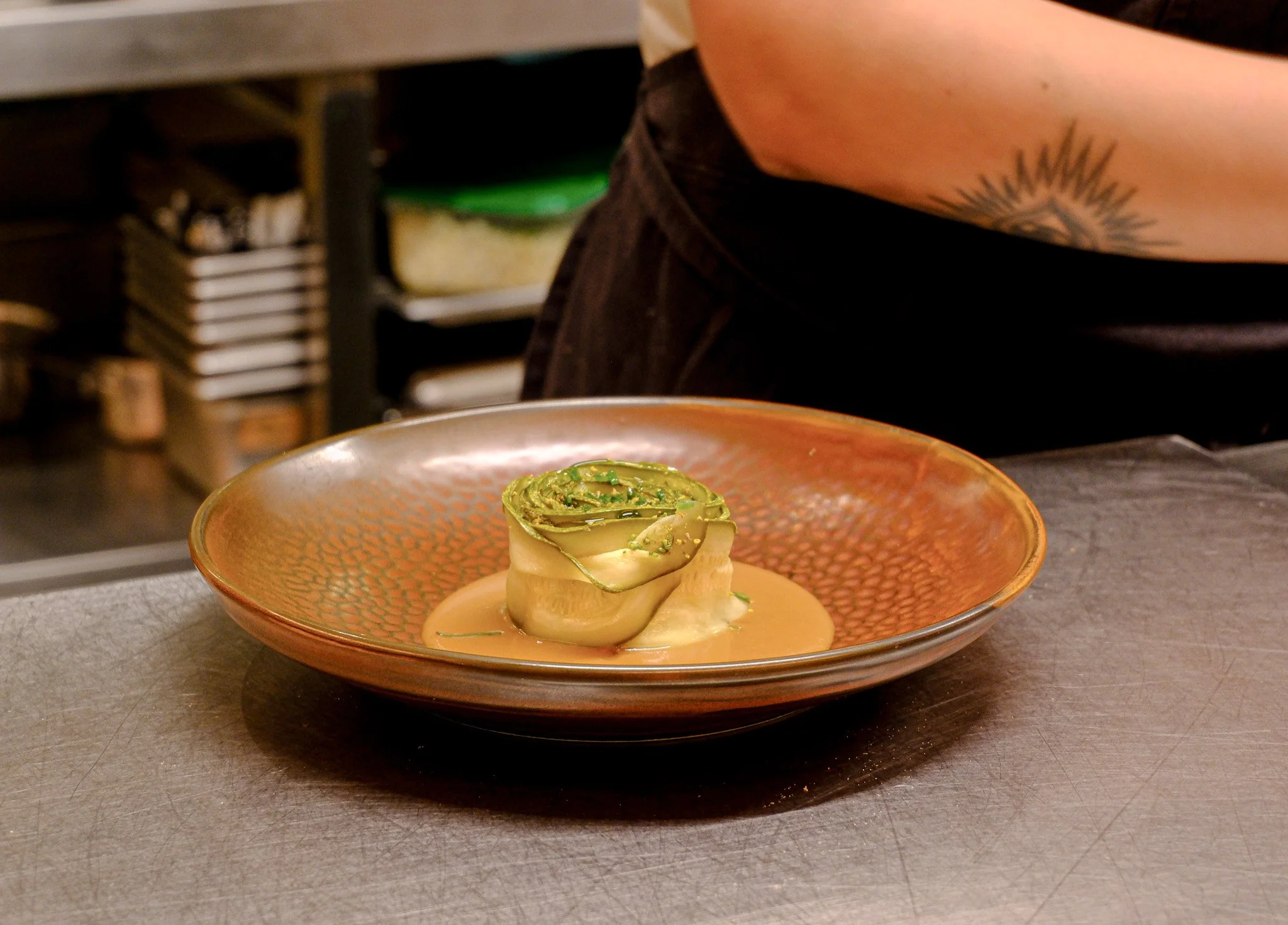 Ein Teller mit einer kunstvoll drapierten Vorspeise, vermutlich mit Avocado und einer lachsfarbenen Sauce, auf einem Küchenarbeitsplatz.