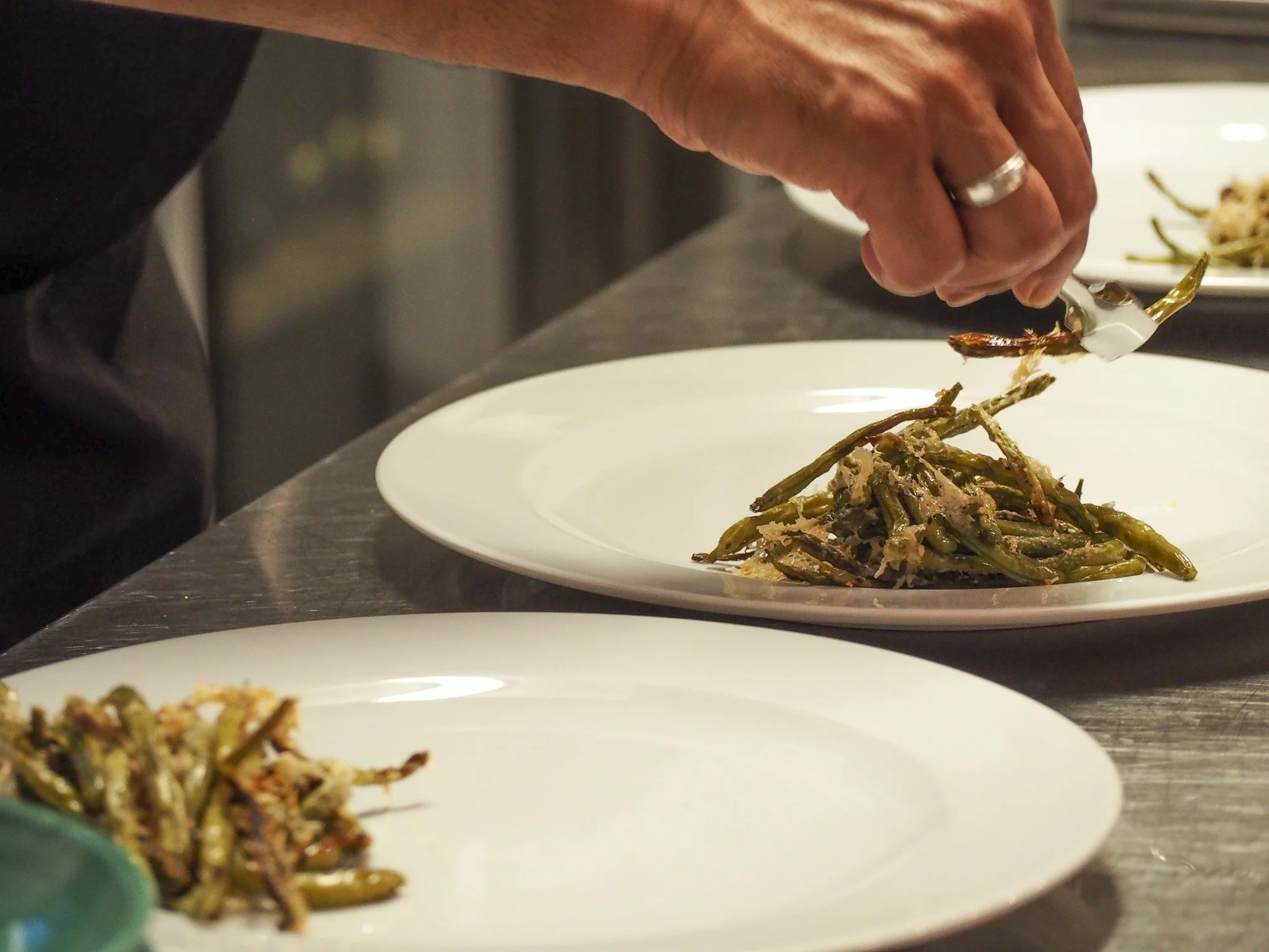 Koch bereitet grüne Bohnen auf einem weißen Teller zu.