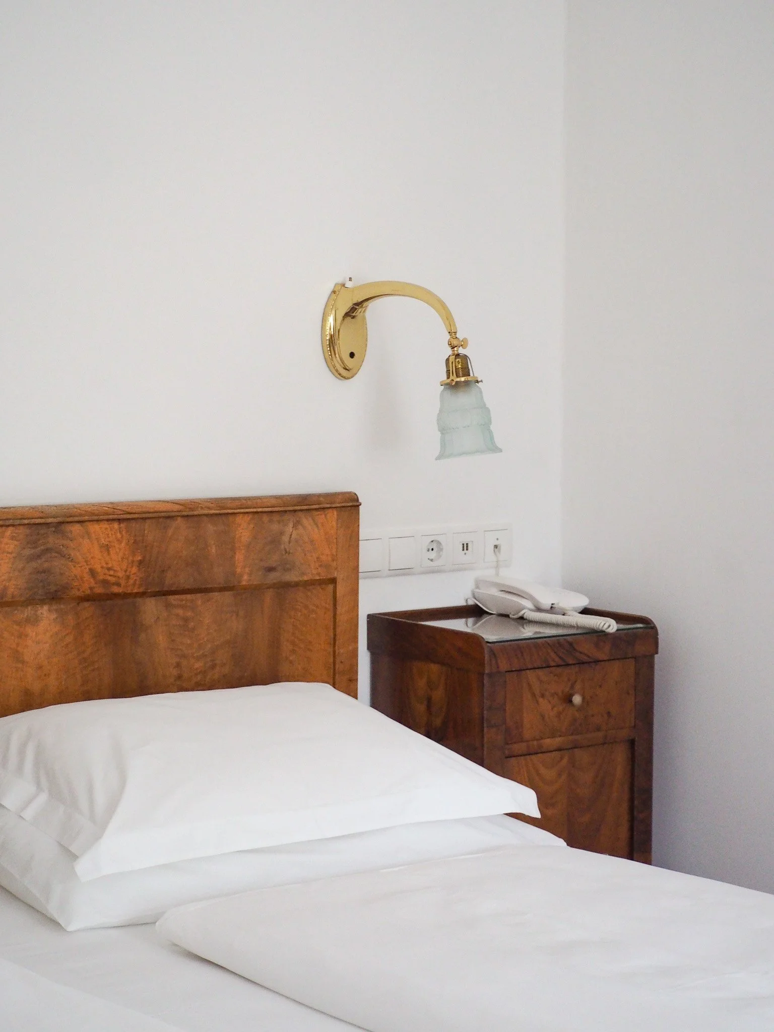 Ein Hotelzimmer mit einem weißen Bett, Holzwandkopfteil, Nachttisch mit Telefon und Wandlampe